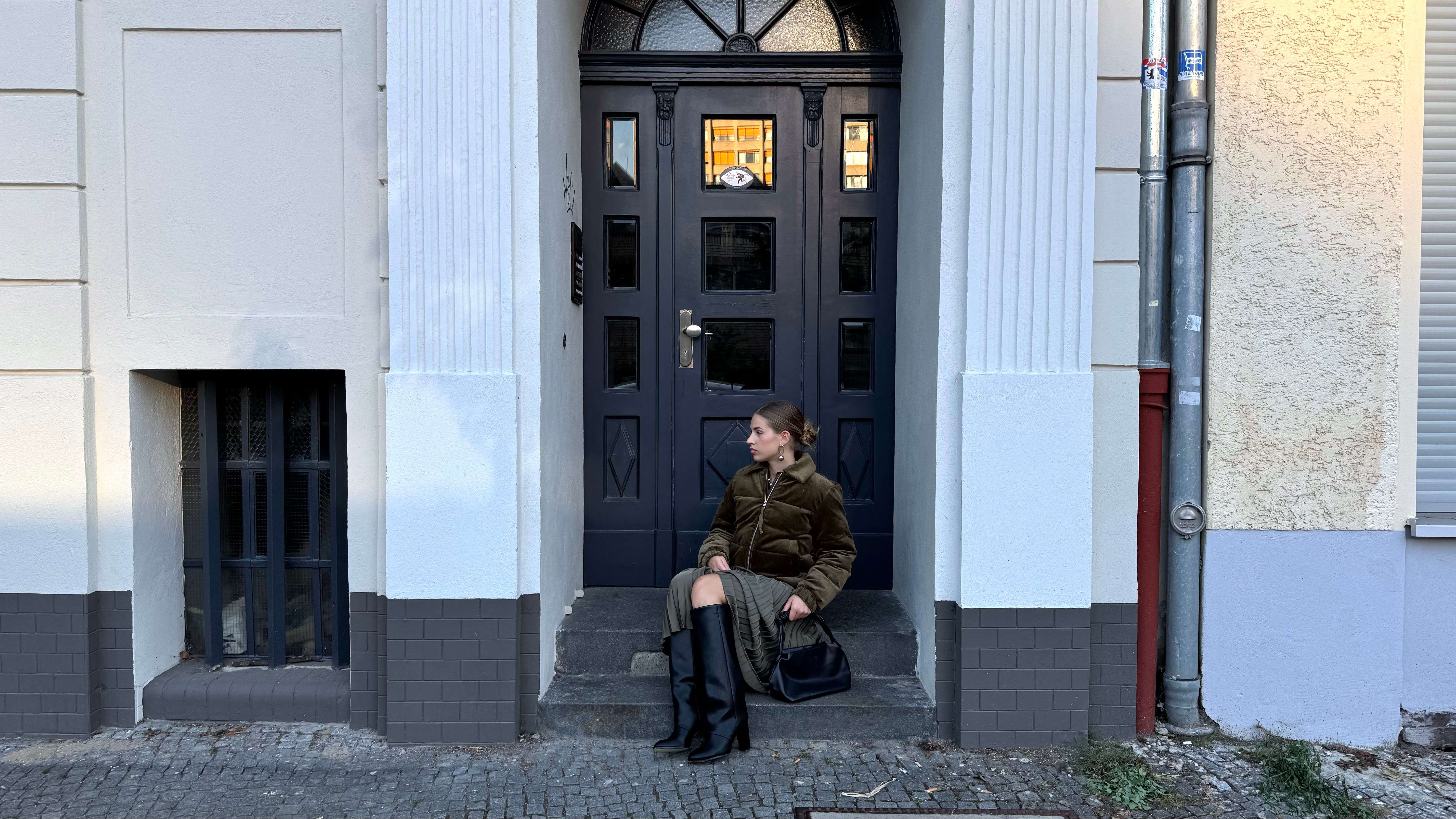 Frau sitzt in Hauseingang, trägt braune Bomberjacke und schwarze Underknee Boots