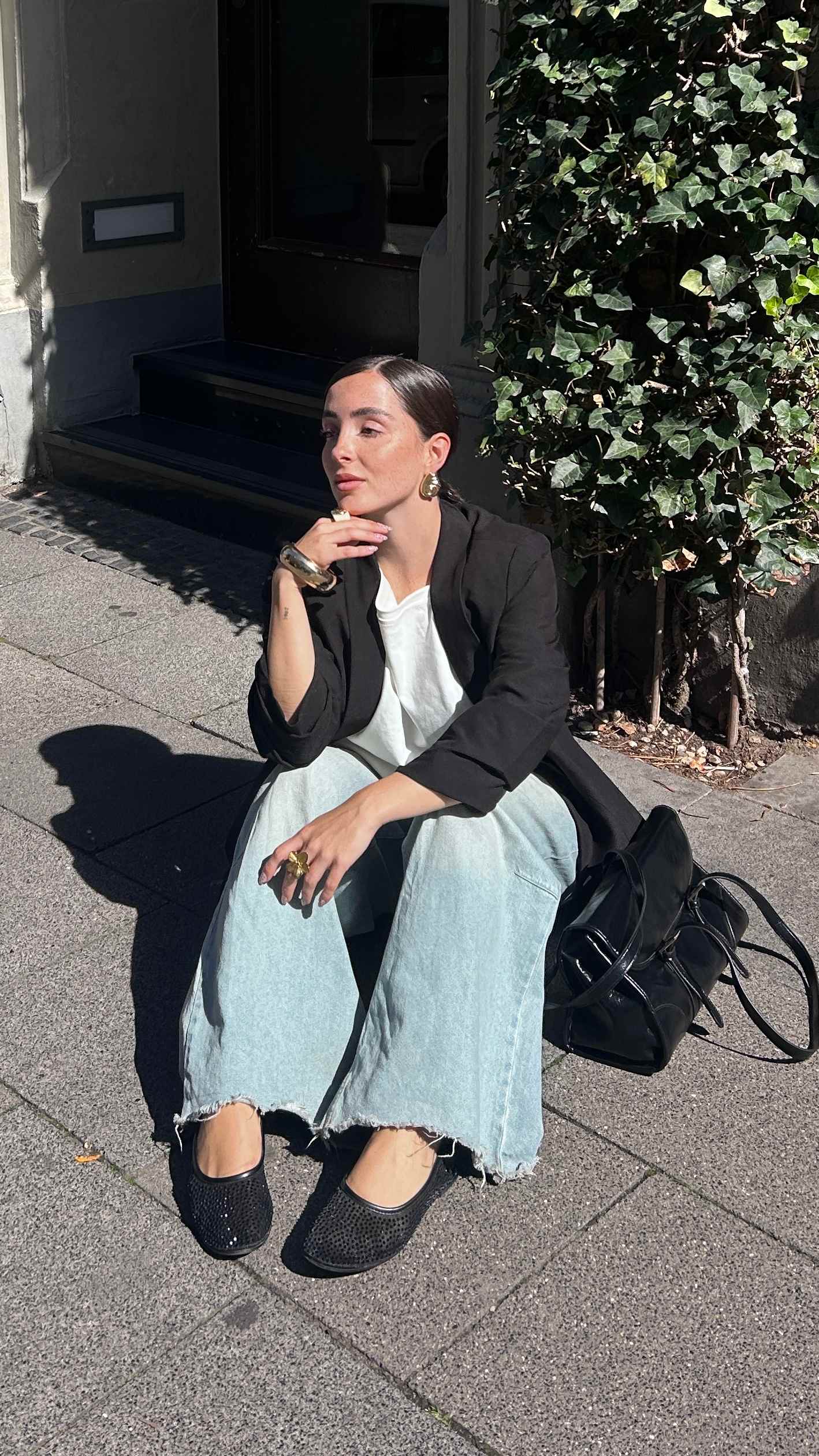 Frau in schwarzem Blazer und Jeanshose sitzt auf Pflastersteinweg