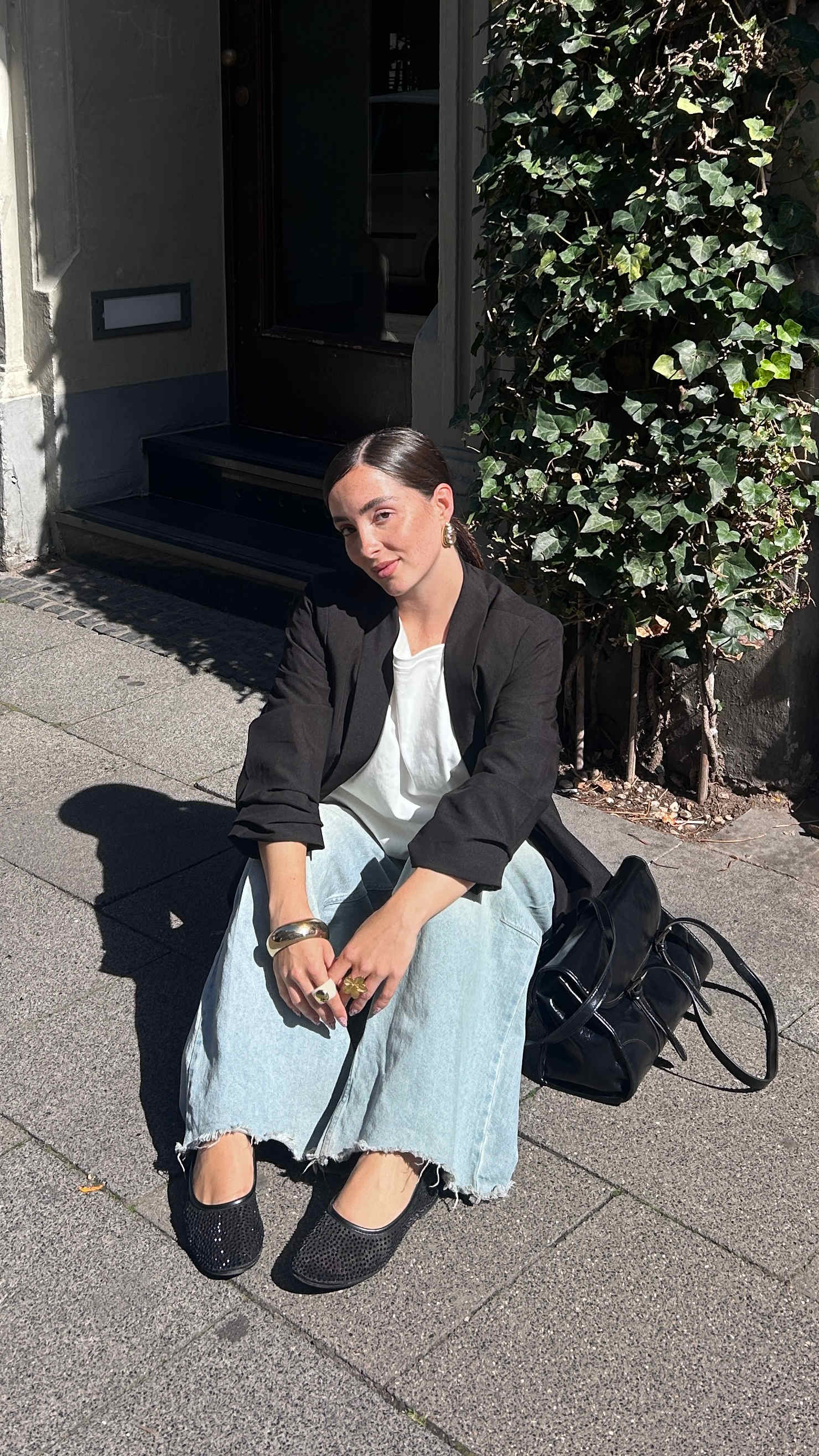 Frau mit schwarzem Blazer und Handtasche, sitzt in strahlendem Sonnenschein auf Fußboden