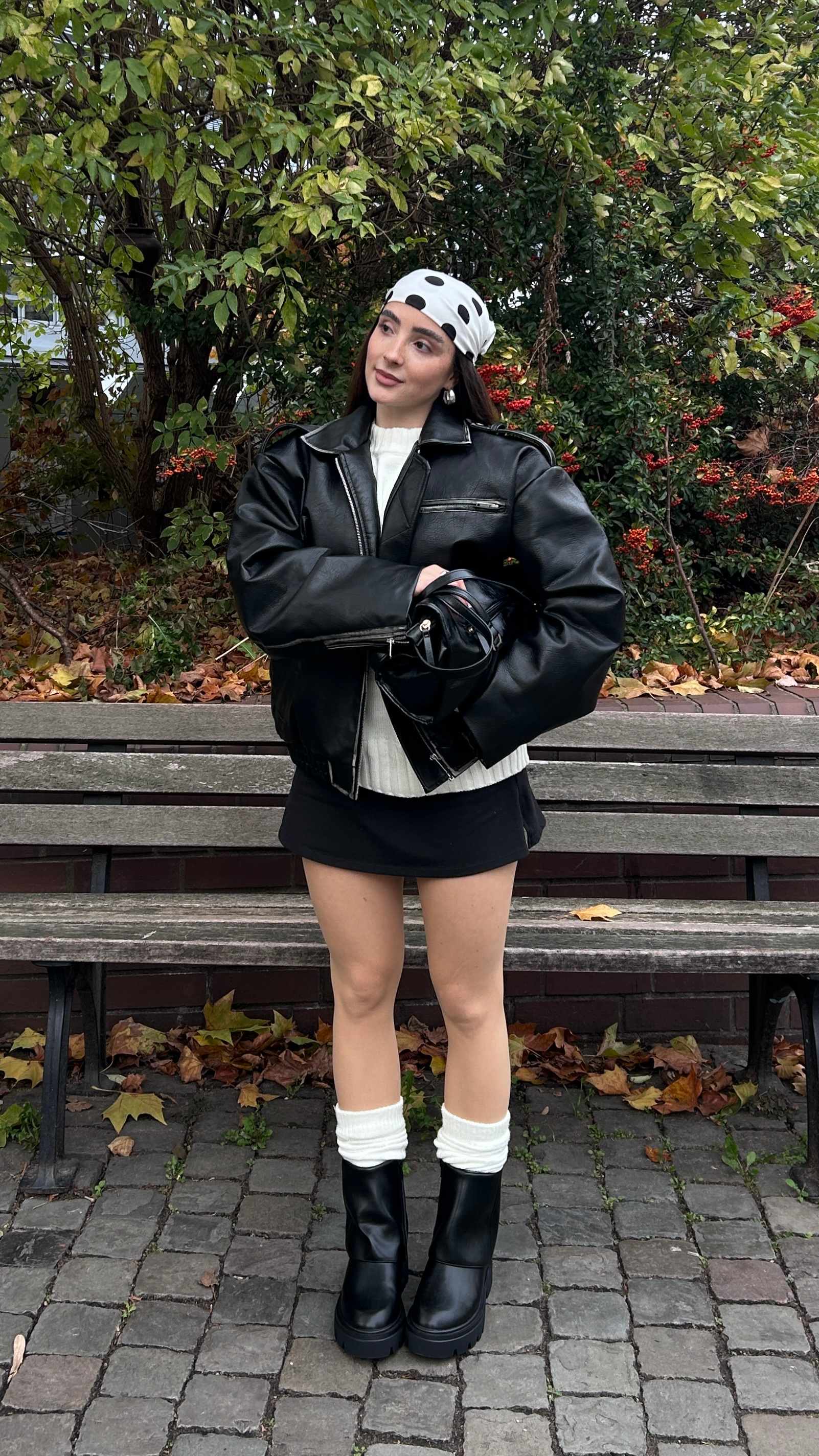 Junge Frau in schwarzem Outfit, bestehend aus Jacke, Minirock und Umschlag-Boots