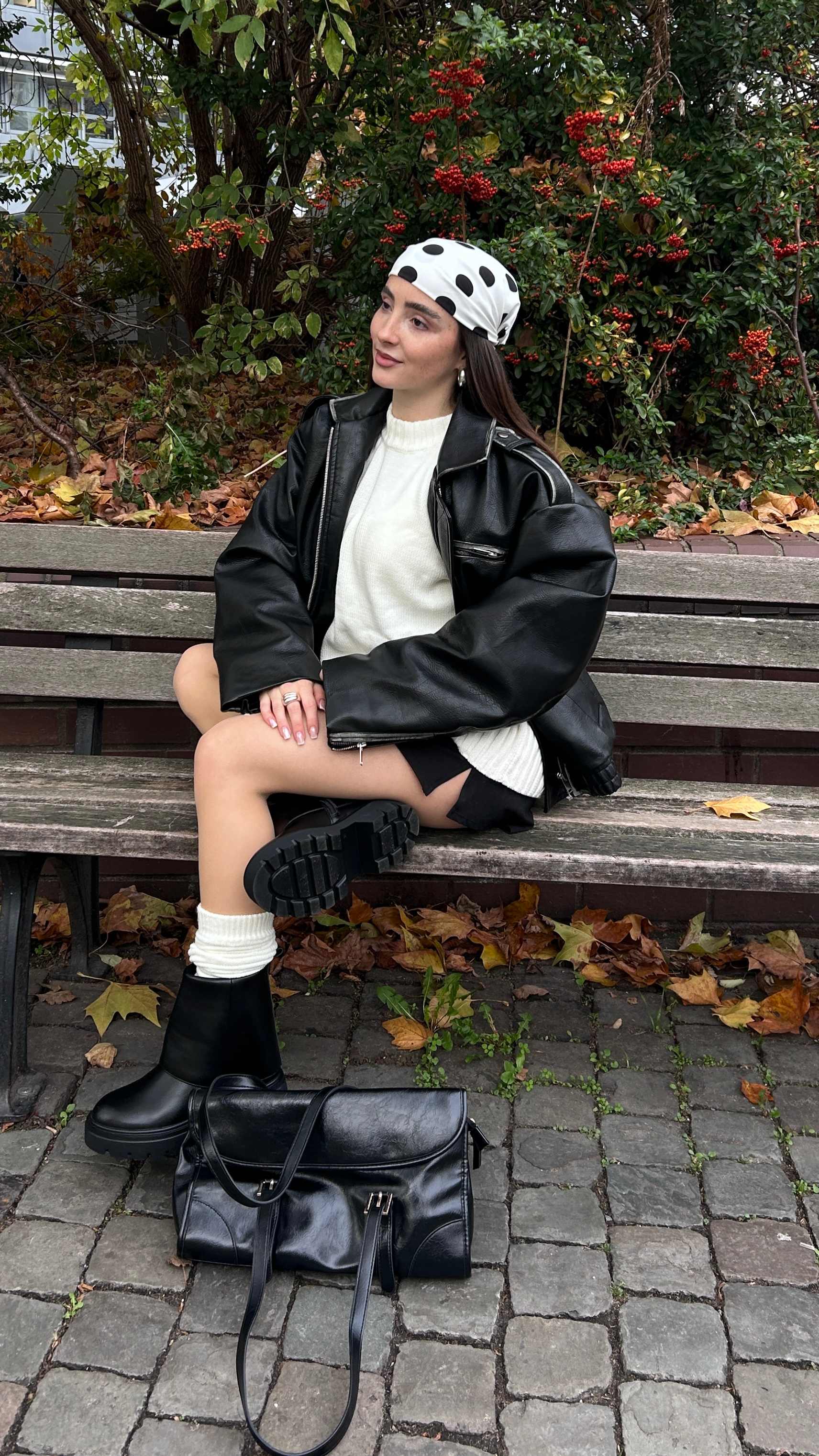 Junge Frau in schwarz-weißem Outfit, trägt Umschlag-Boots, sitzend auf Parkbank