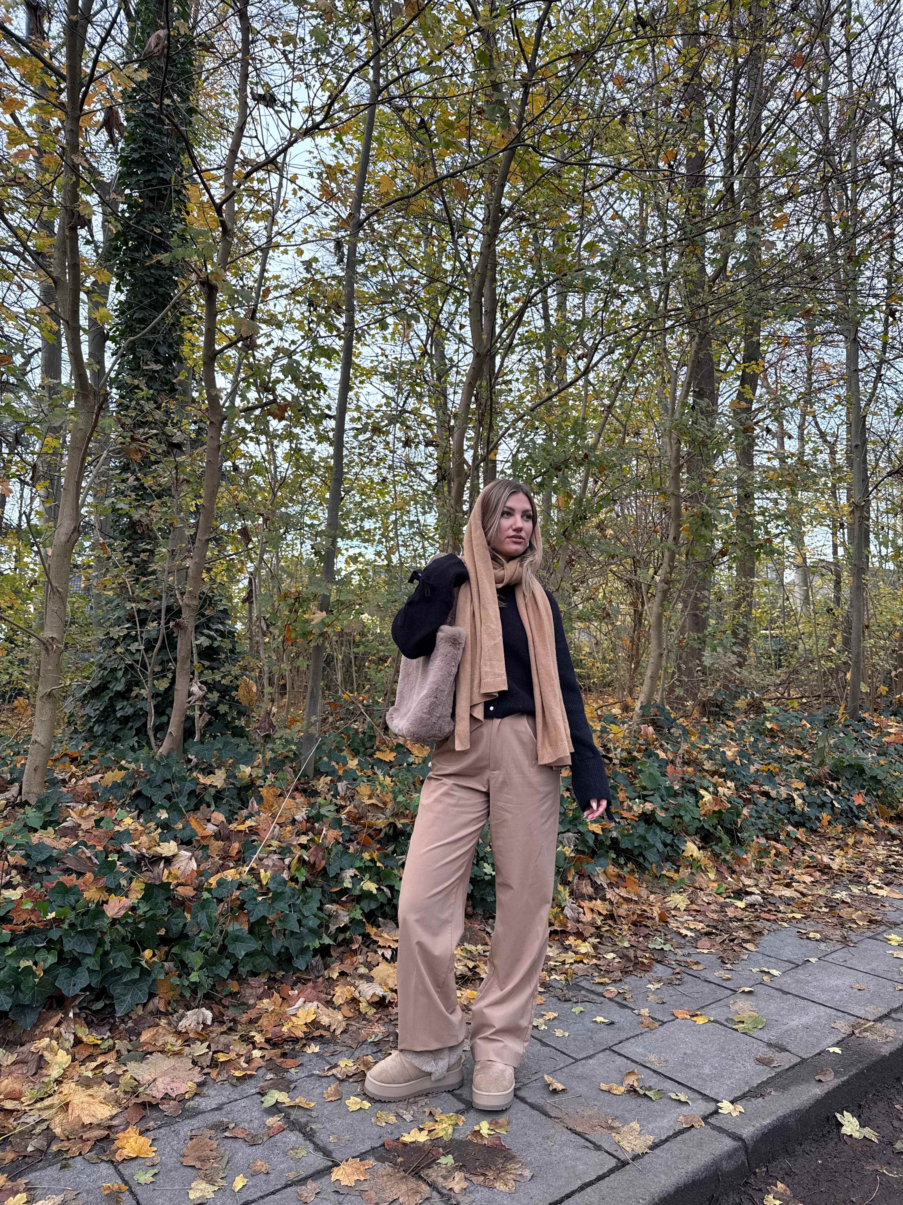 Frau in lässigem Kuschel-Outfit mit schwarzem Cardigan-Top, steht auf Waldweg