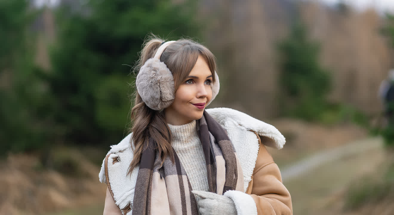 Frau in braun-weißem Fellmantel trägt graue Ohrenwärmer in flauschiger Optik