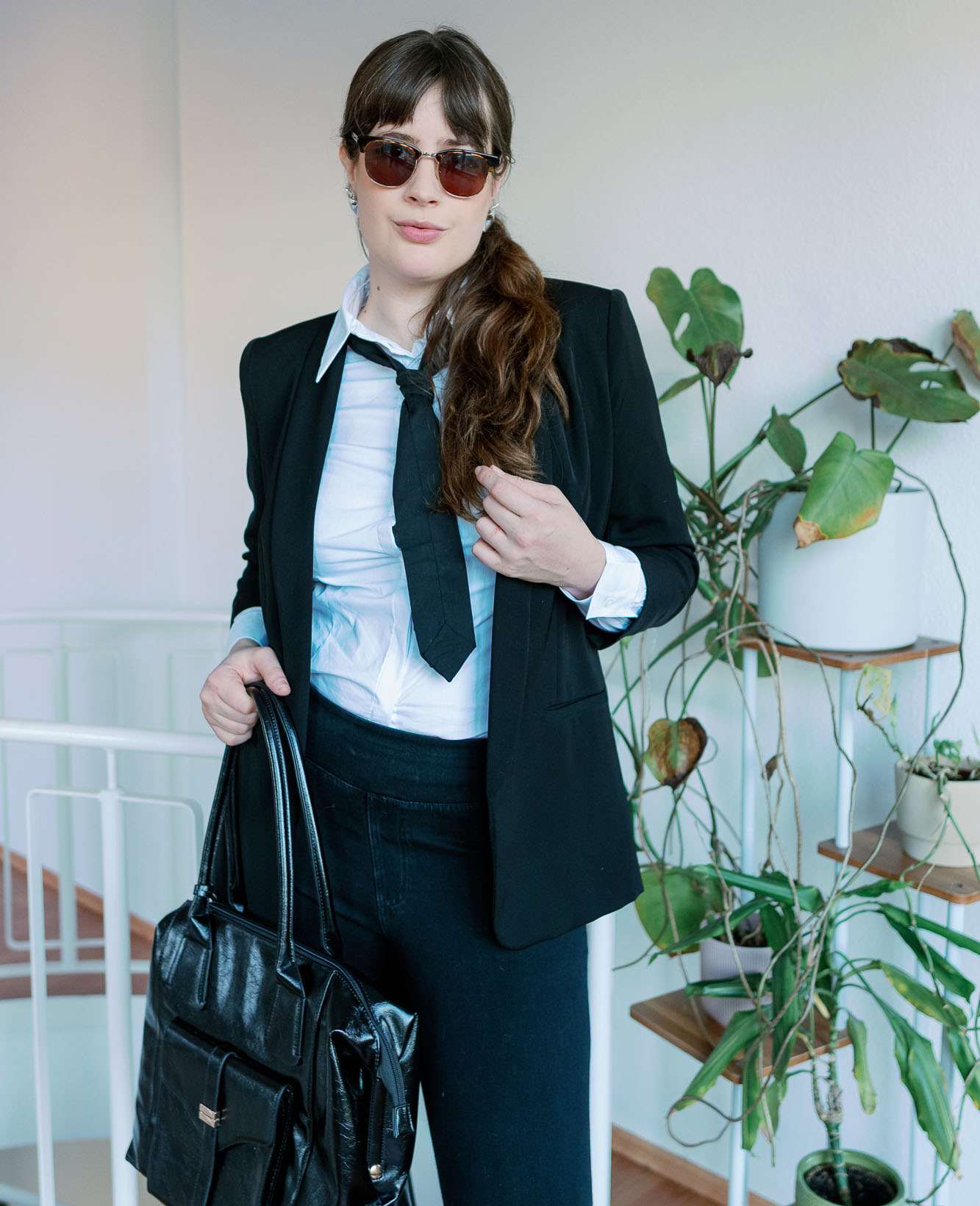 Frau mit lockigem Haar, posiert in Karl Lagerfeld-Kostüm, kombiniert mit schwarzer Handtasche