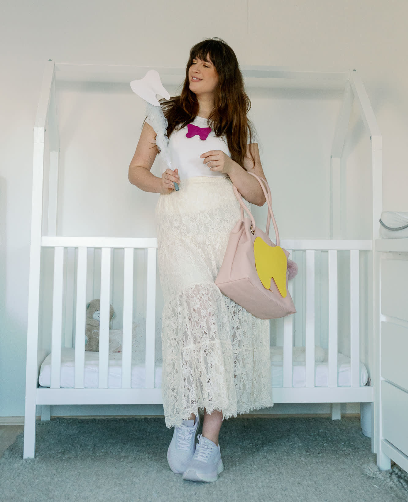 Frau in weißem Zahnfee-Kostüm zu Karneval, steht vor Babykrippe