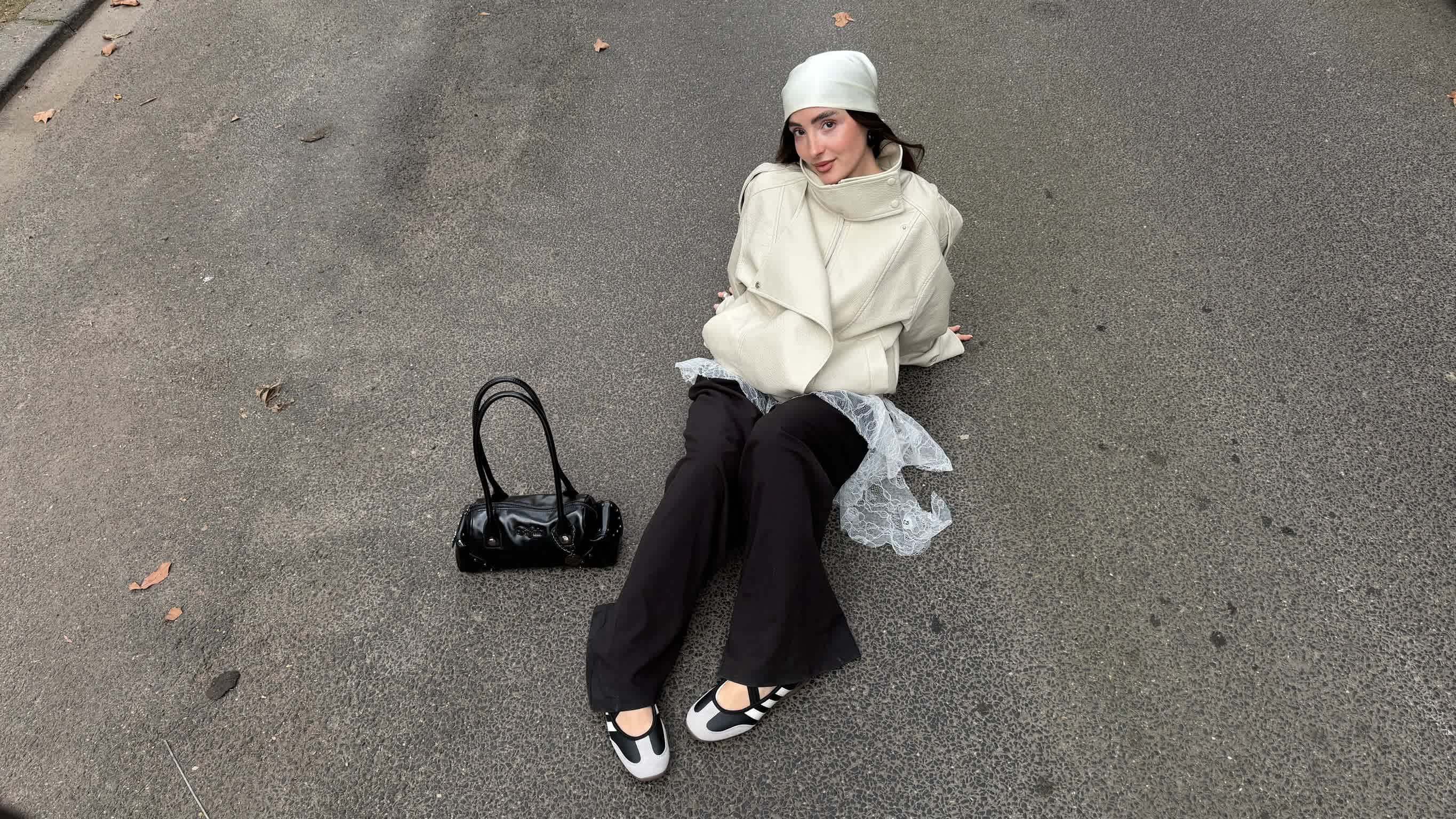 Frau in cremefarbener Oversize-Lederjacke und weiter schwarzer Hose. Im Fokus: Schwarz-weiße Riemchen-Ballerinas im sportlichen Look.
