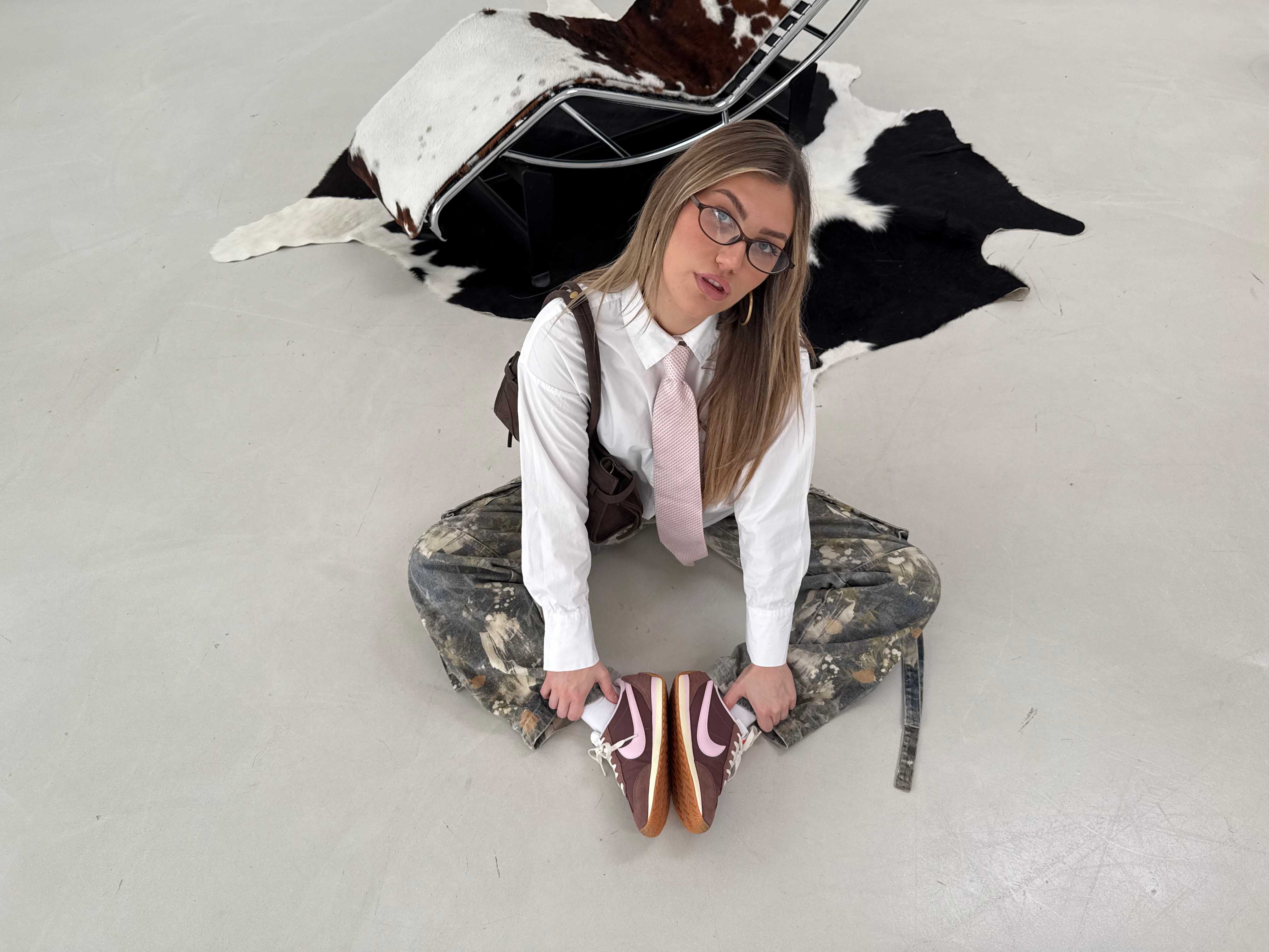 Frau in grauem Hosenträger-Outfit mit weißem Shirt und Krawatte, sitzend am Boden