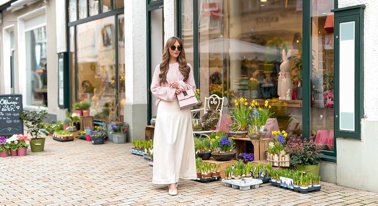 Junge Frau in pastellfarbenem Outfit steht vor Blumengeschäft
