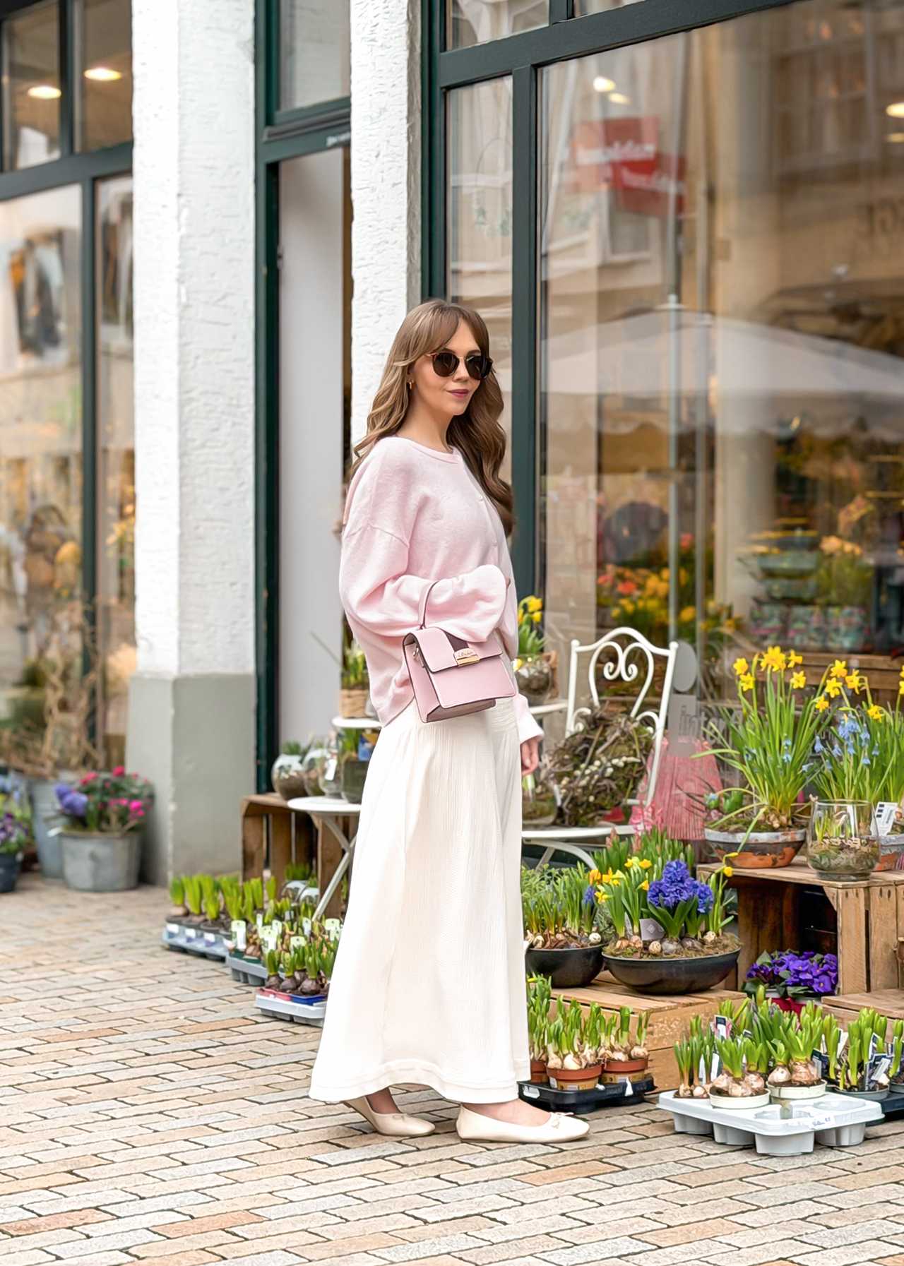 Frau in pastellfarbenem Brunch Outfit, stehend vor Auslage eines Blumengeschäfts