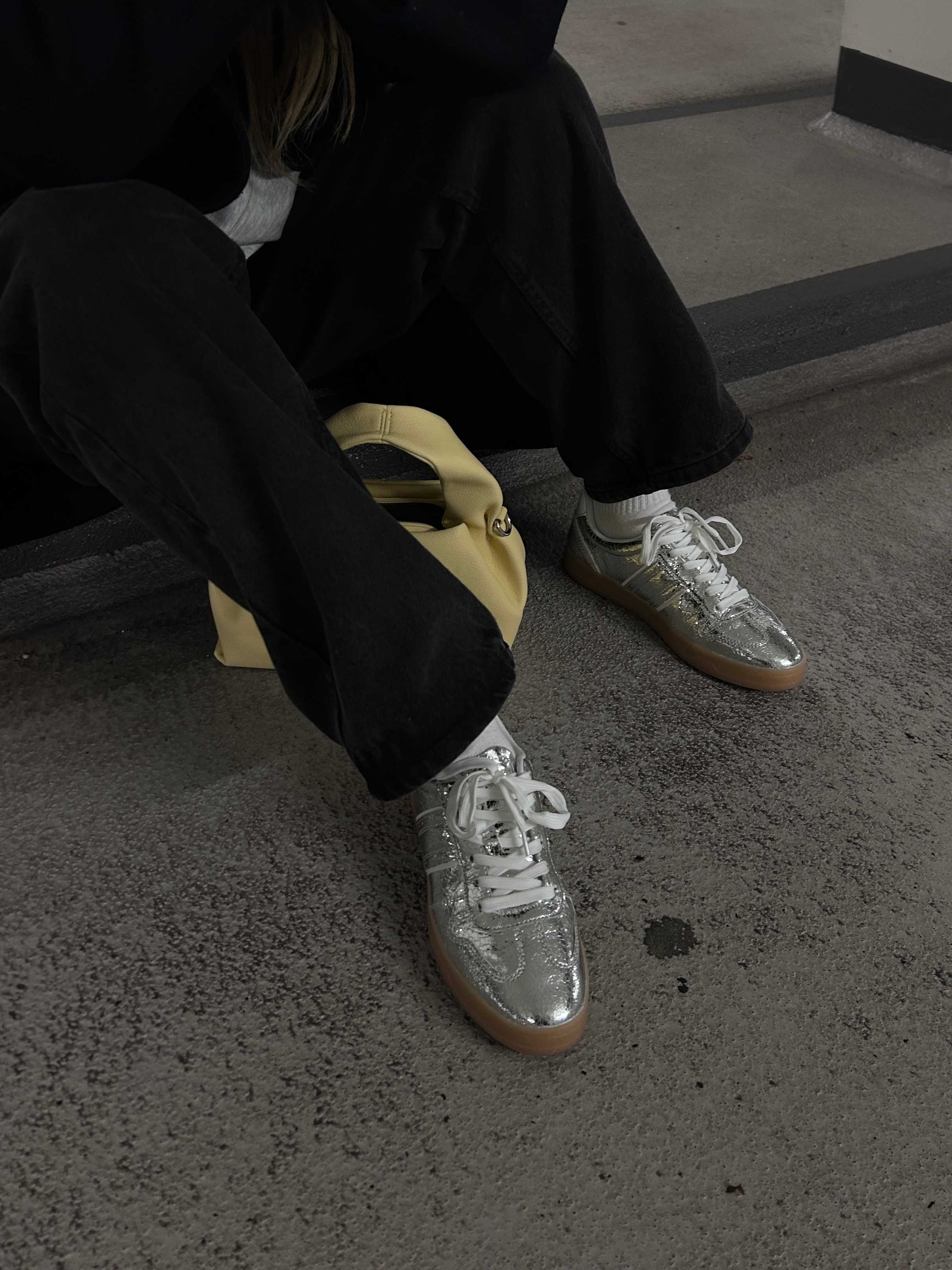 Frau trägt schwarze Hose mit silbernen Metallic Sneakern