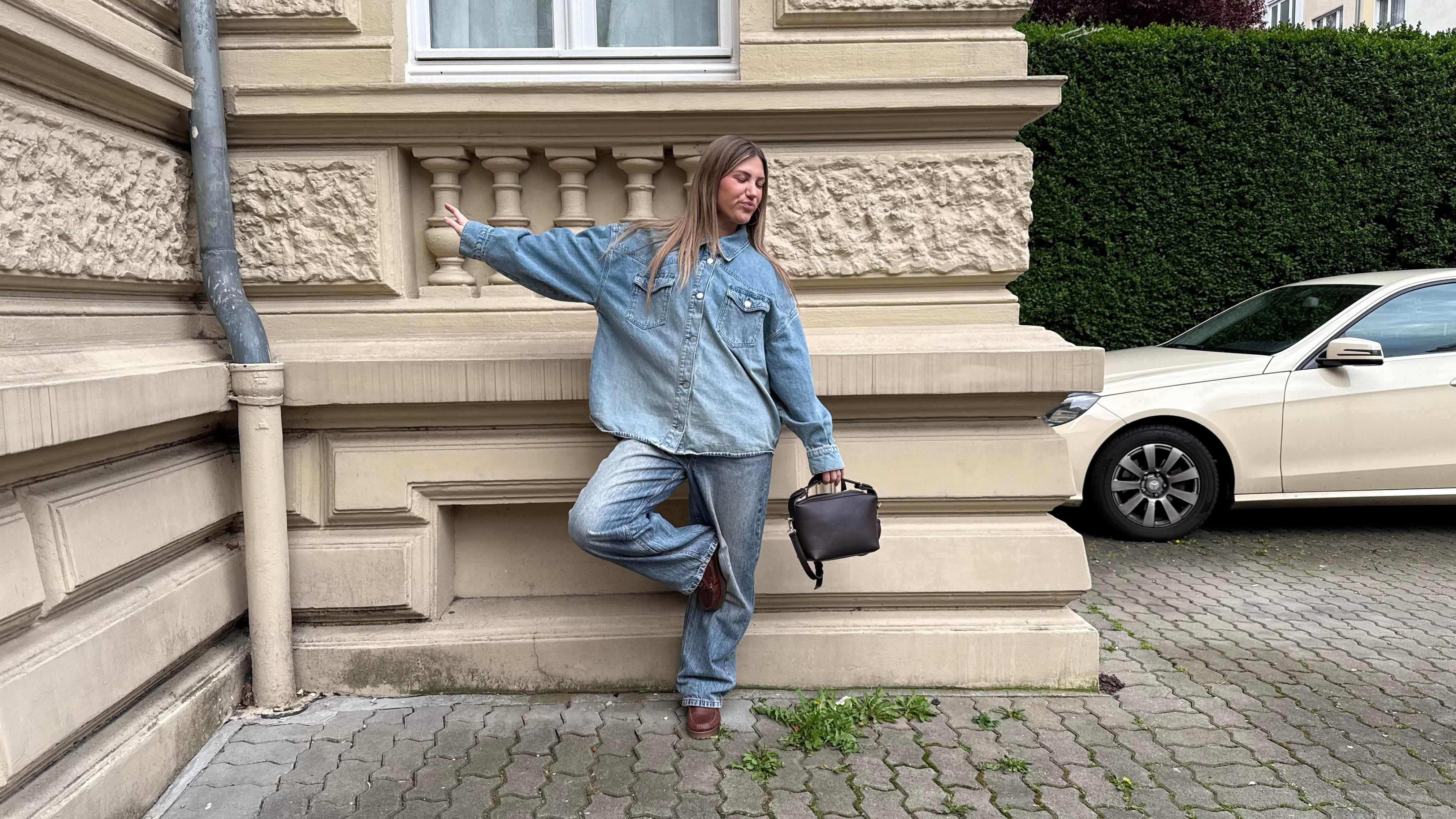 Junge Frau im All-over-Denim-Look, steht vor Hauswand, trägt Bootsschuhe