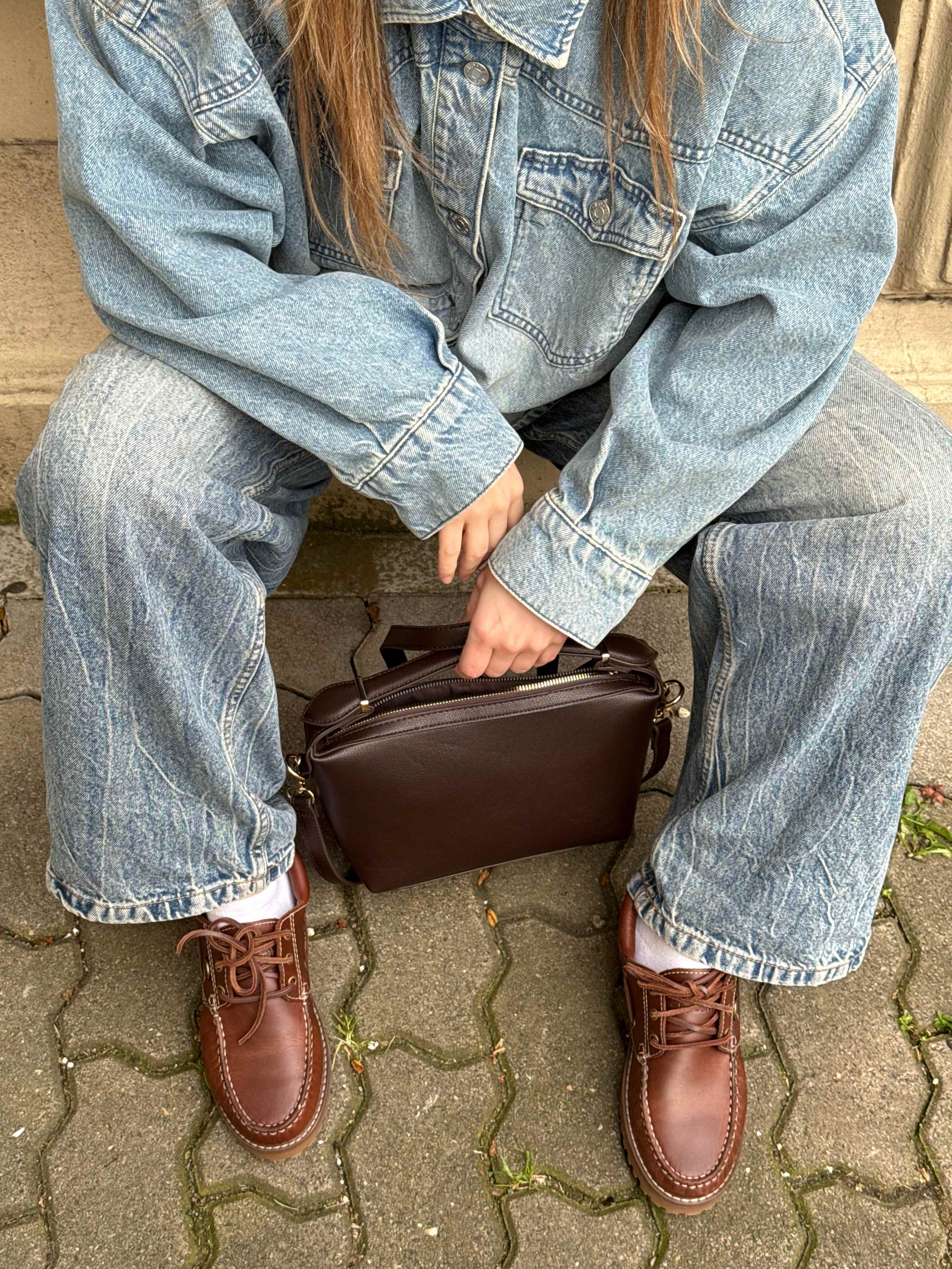 Top-Down-Sicht auf eine Frau in Denim-Outfit, kombiniert mit braunen Bootsschuhen und passender Handtasche
