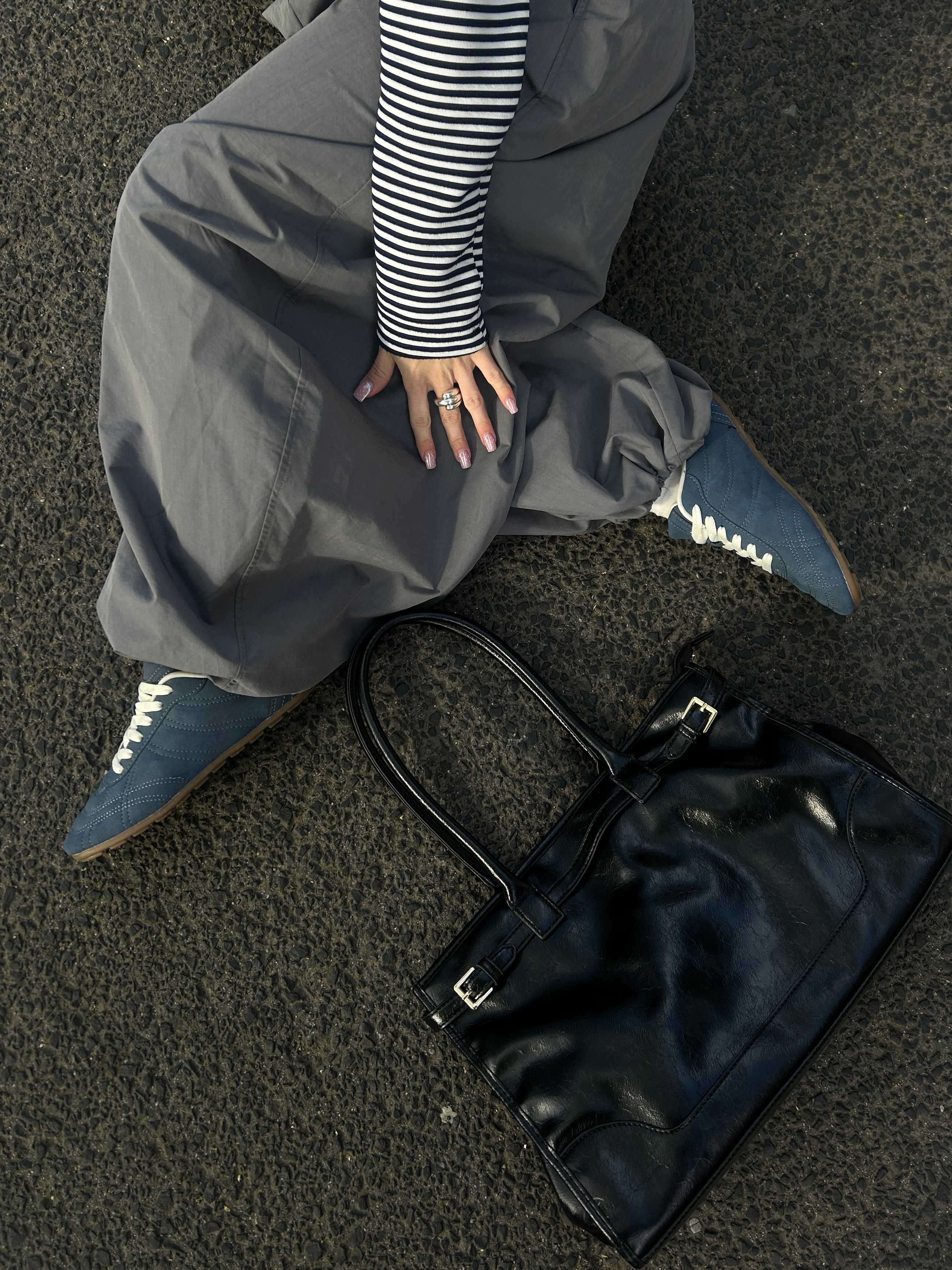 Frau auf Steinboden, in grauem Outfit, mit silbernen Y2K-Sneakern und schwarzer Handtasche