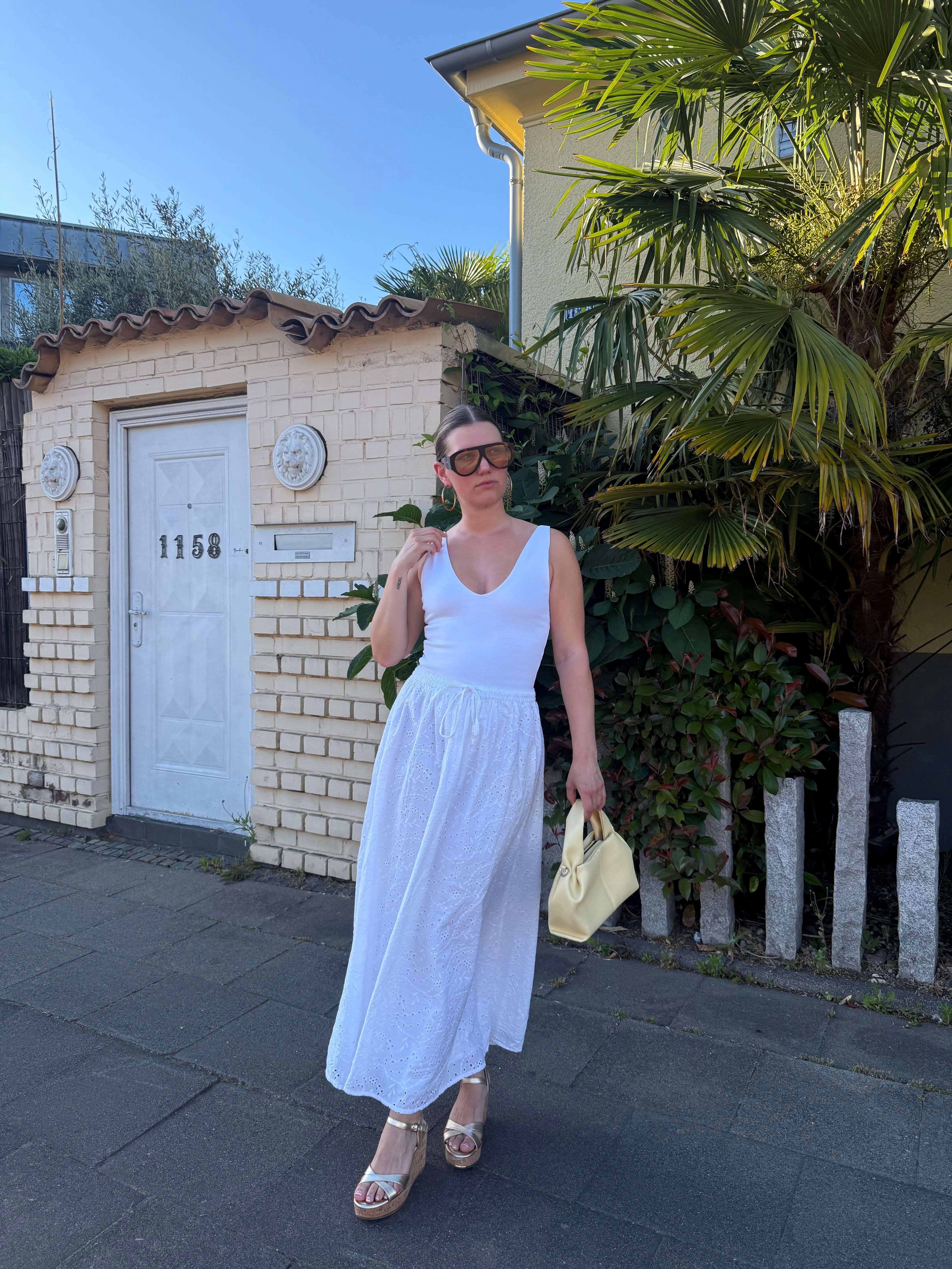 Frau präsentiert lockeres sommerliches Outfit mit weißem Kleid und Kork Wedges