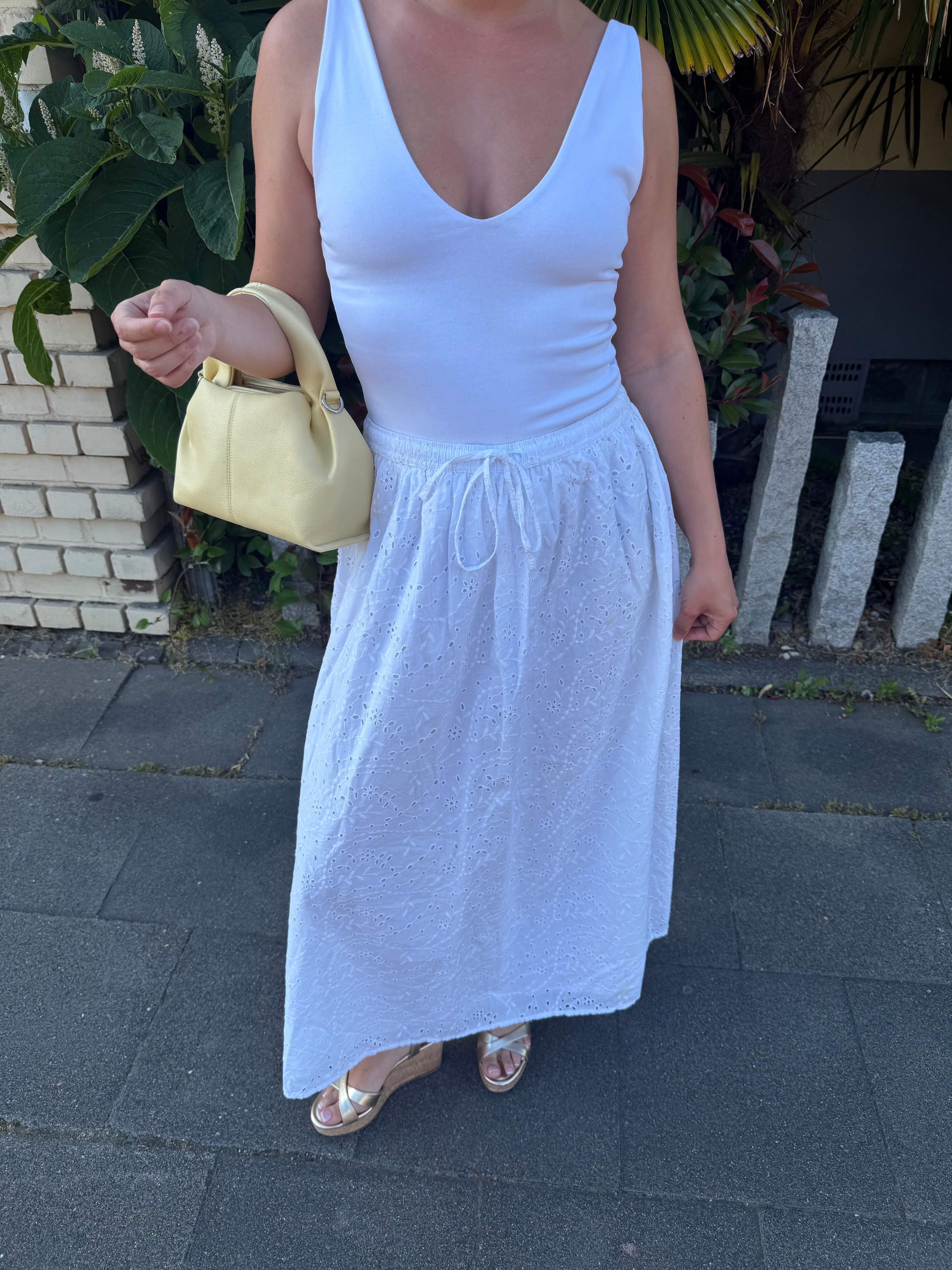 Frau präsentiert sommerliches Outfit mit weißem Kleid, goldenen Details und Kork Wedges