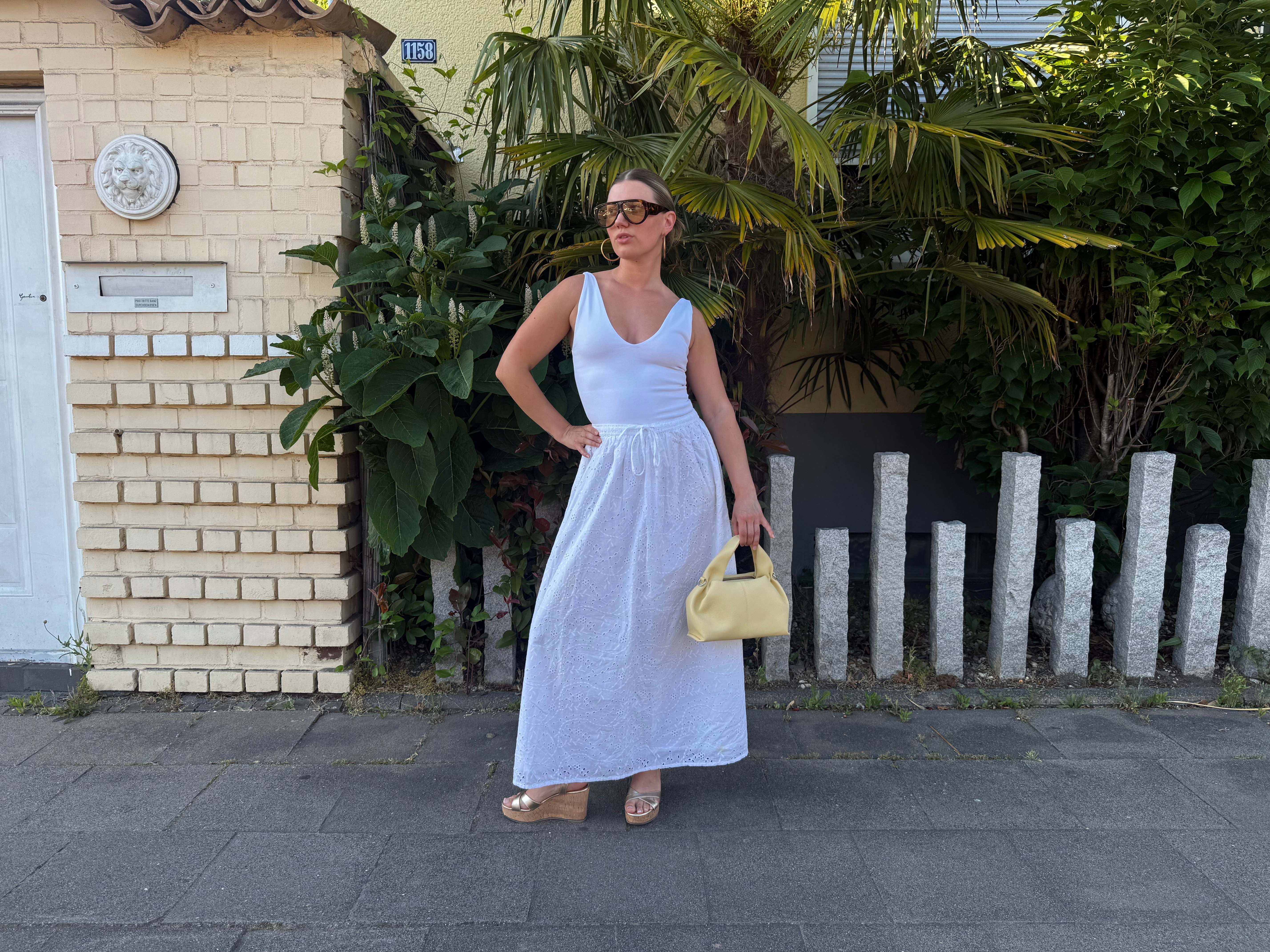 Frau zeigt komplettes Sommer-Outfit mit Kork Wedges, gelber Handtasche und Statement-Brille