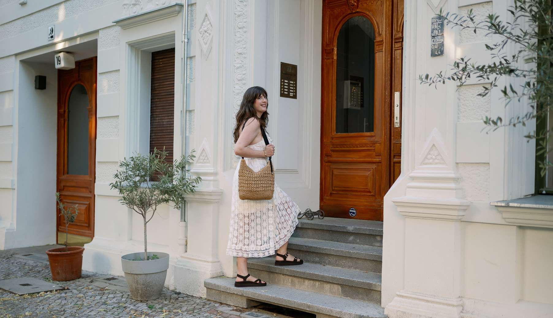 Frau in weißem Hemdkleid, trägt beige Basttasche, steigt Treppenstufen
