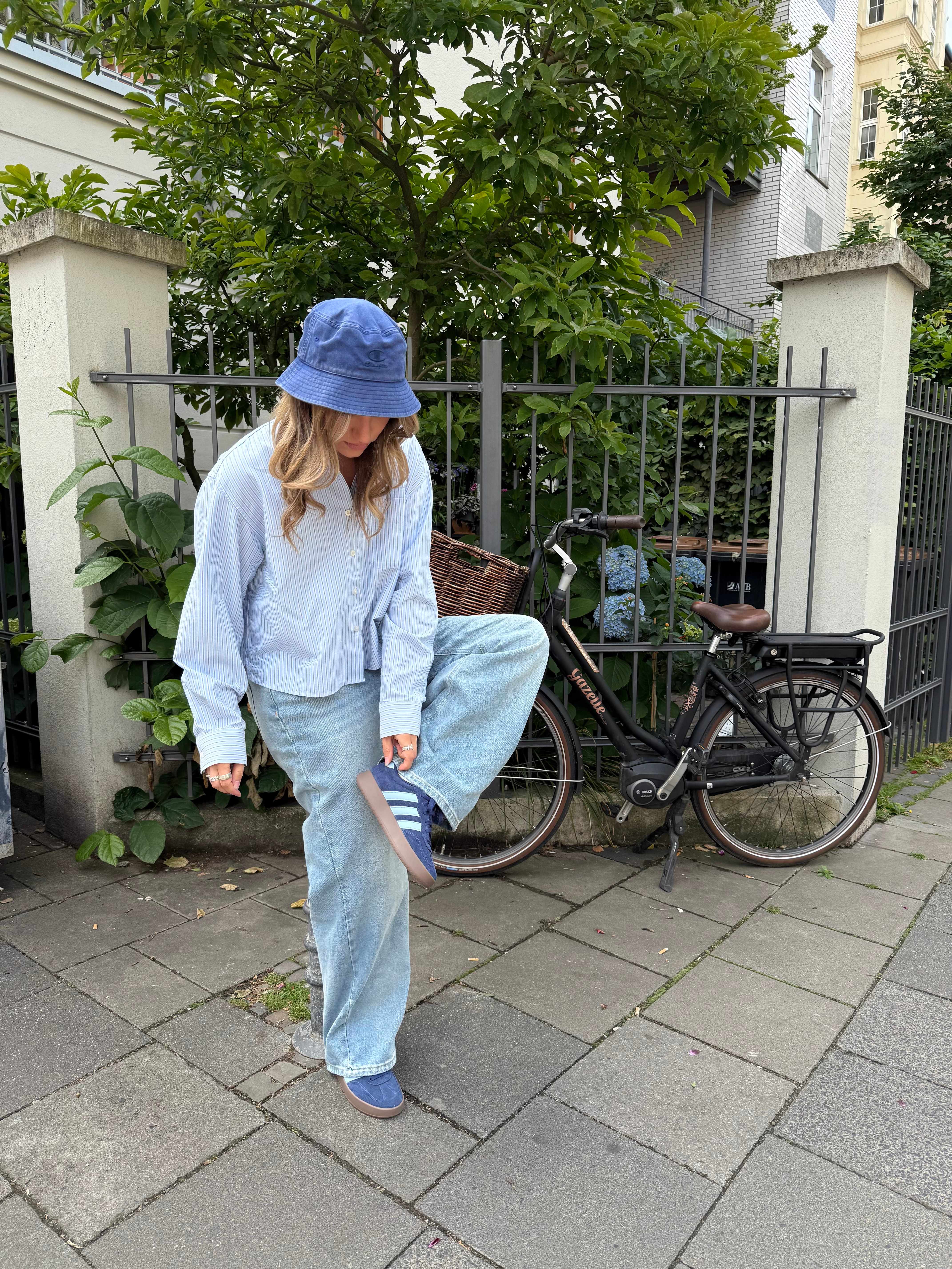 Frau zeigt Outfit mit Bucket Hat und passenden blauen Adidas Sneakern