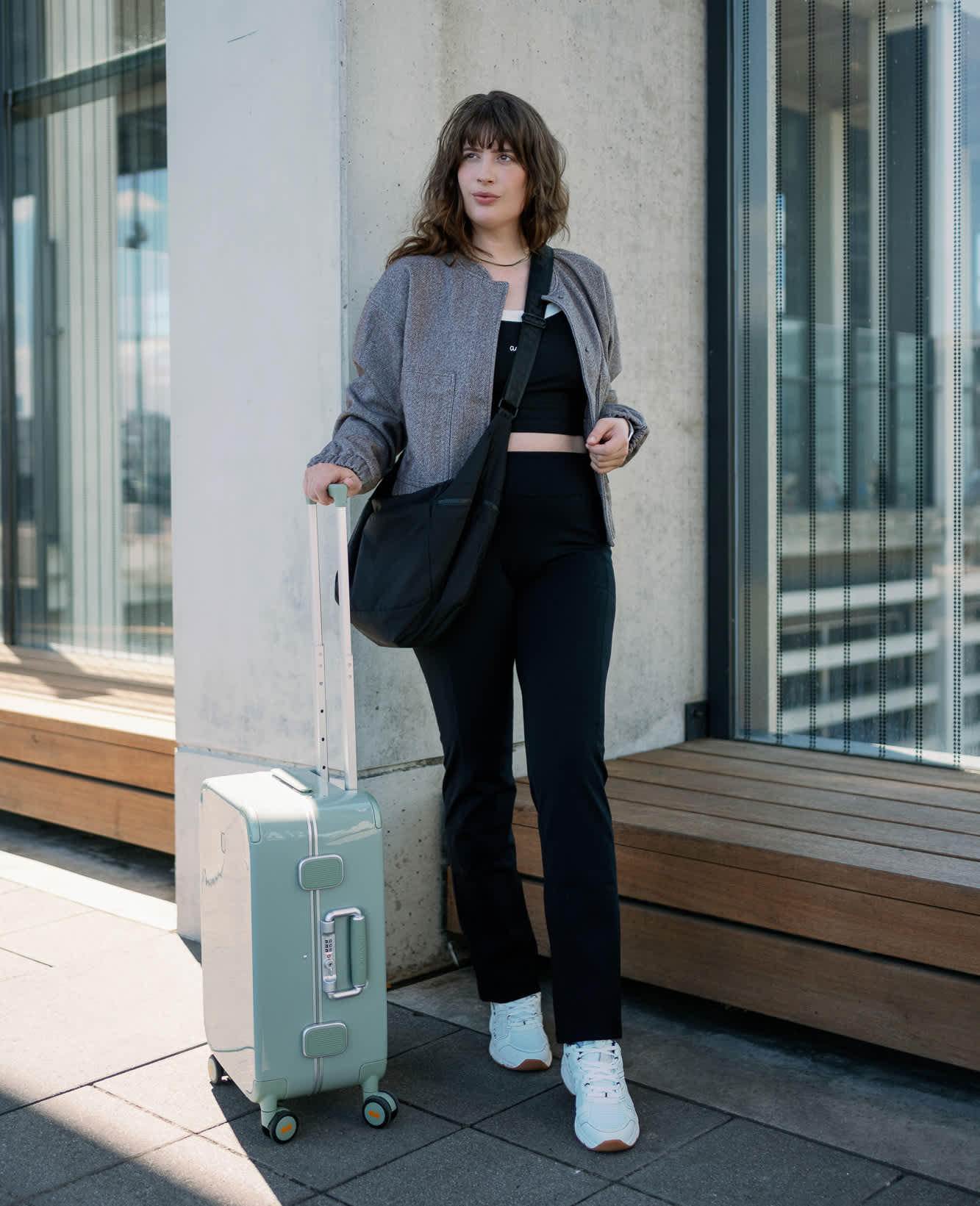Frau in schwarzem Flugzeug-Outfit mit grauer Überjacke und Rollkoffer an der Hand