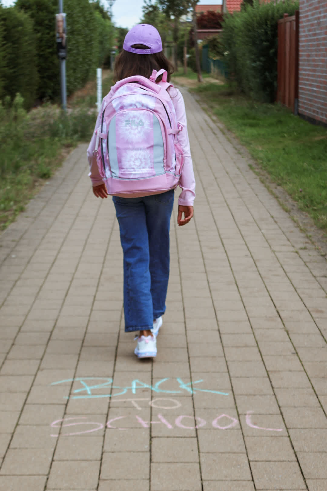 Kind mit rosa Fila-Rucksack läuft über Gehweg mit Kreideschrift Back to School