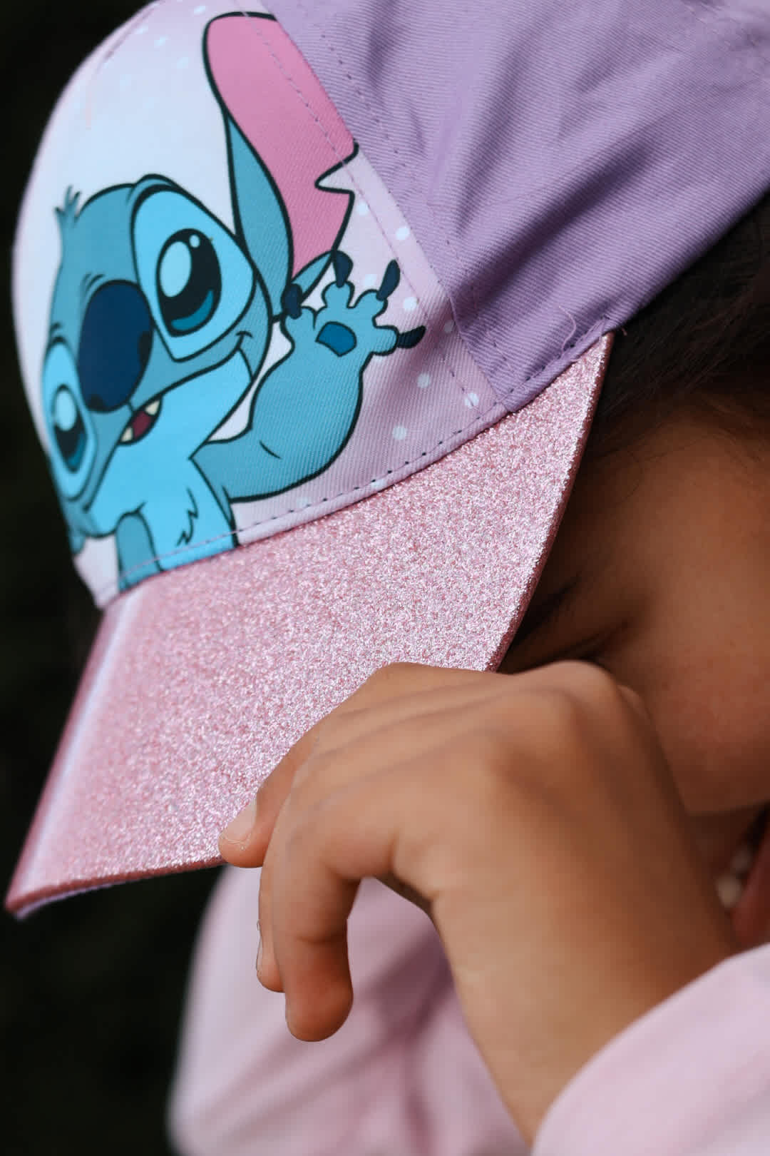 Kind trägt lila Kinderkappe mit Comic-Print und glitzerndem rosa Schirm