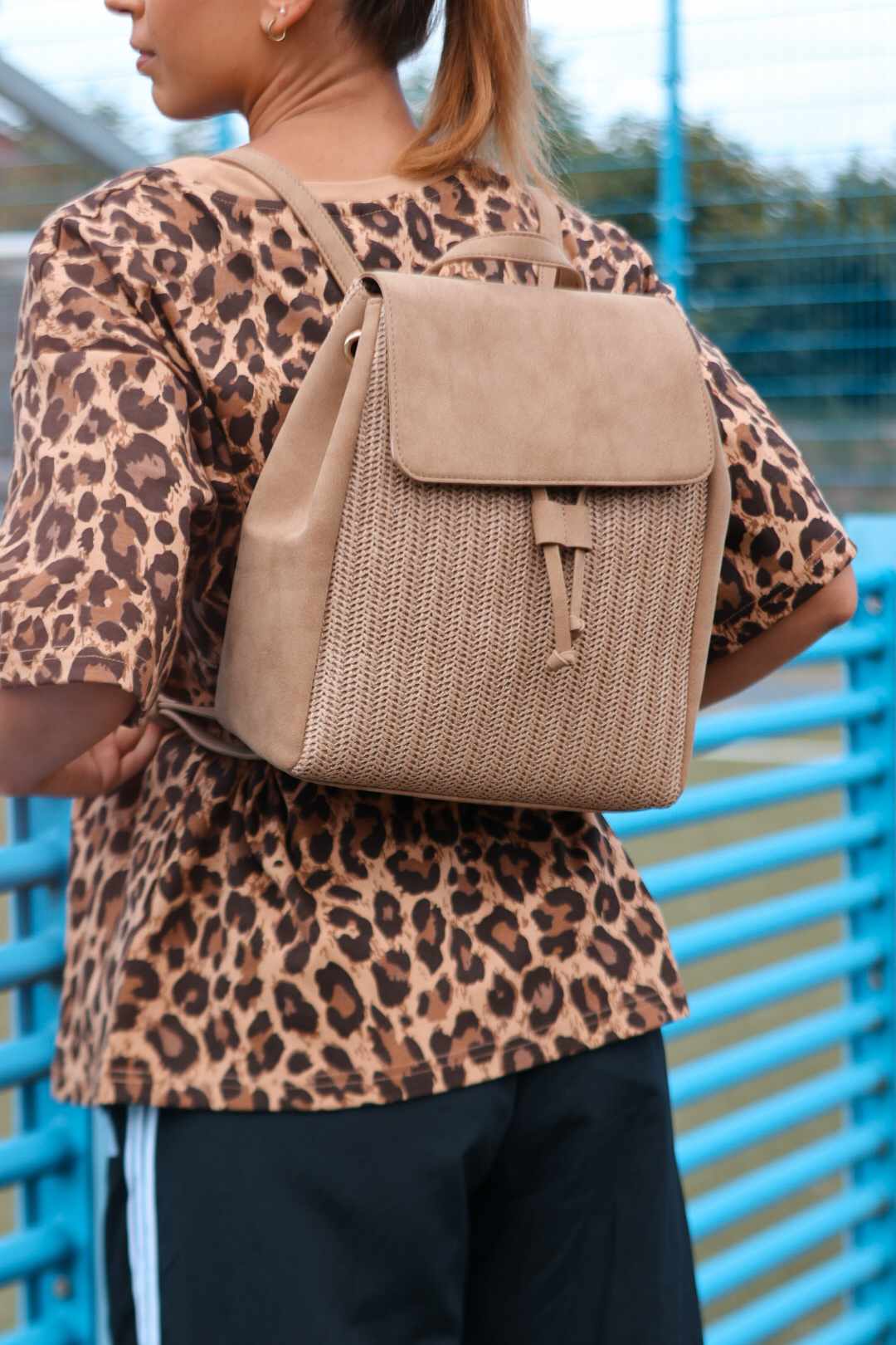 Junge Frau trägt beigen Flechtrucksack mit Klappe über Leo-Print-Shirt