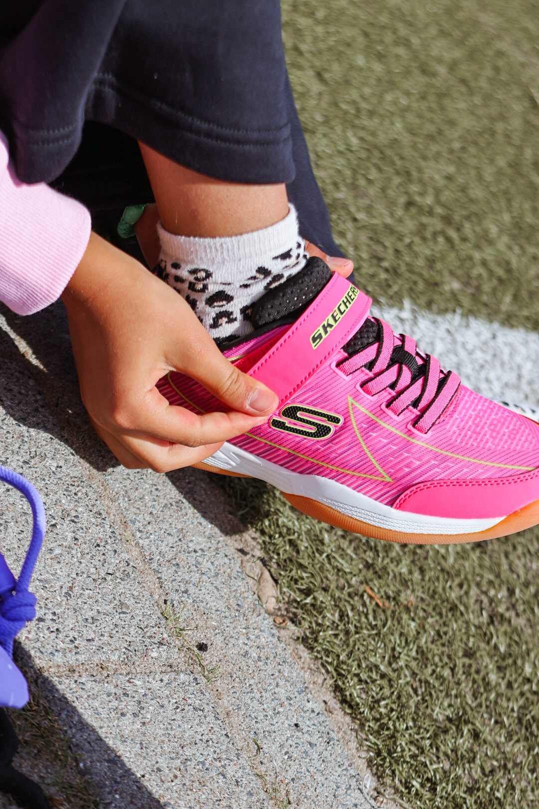 Kind schließt Klettverschluss eines pinken Skechers-Sneakers, trägt dazu Leopardensocken