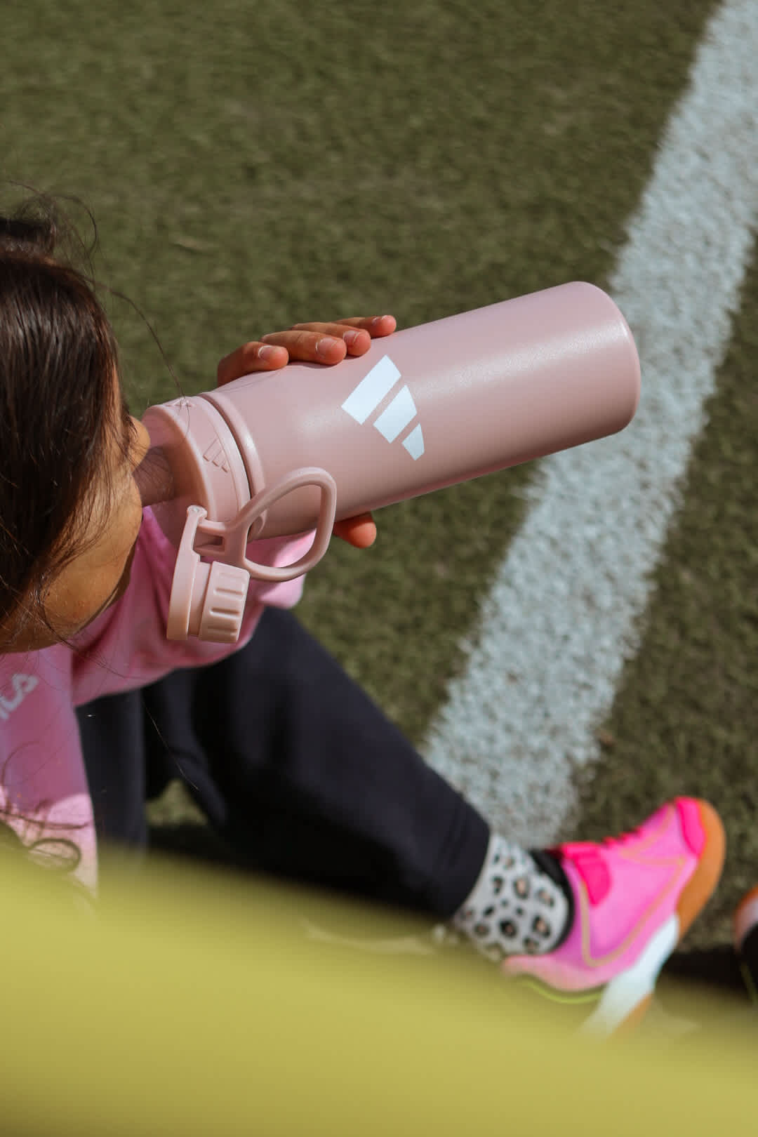 Kind trinkt aus rosa Adidas-Trinkflasche am Spielfeldrand mit pinken Sneakern