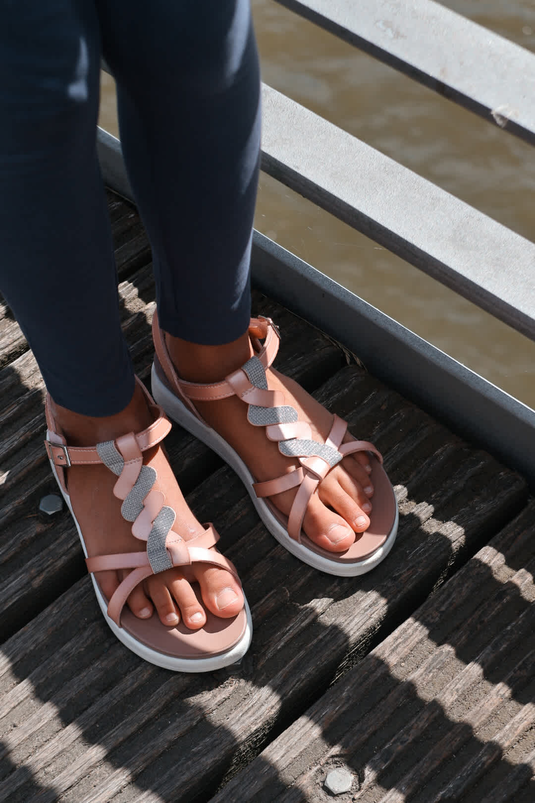Nahaufnahme von rosa Riemchensandalen mit Glitzerdetail auf einem Holzsteg