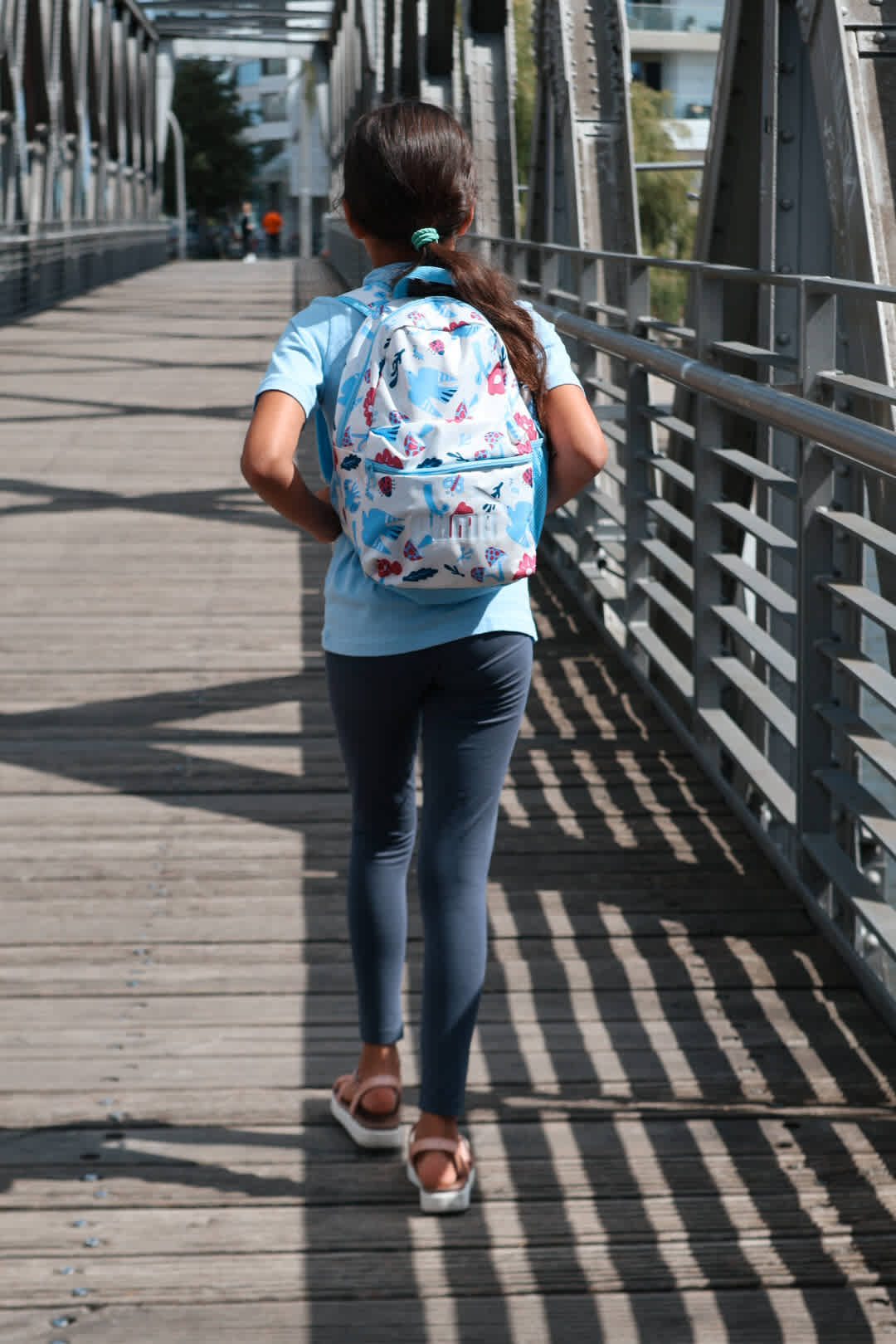 Kind mit buntem Rucksack und Sandalen in Back to School-Outfit läuft über eine Fußgängerbrücke