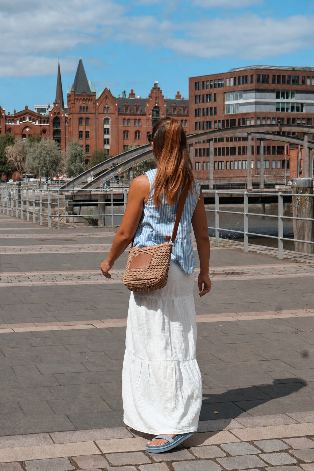 Frau trägt Sommer-Look mit gestreiftem Top, weißem Maxirock und Korbtasche vor Speicherstadt-Kulisse