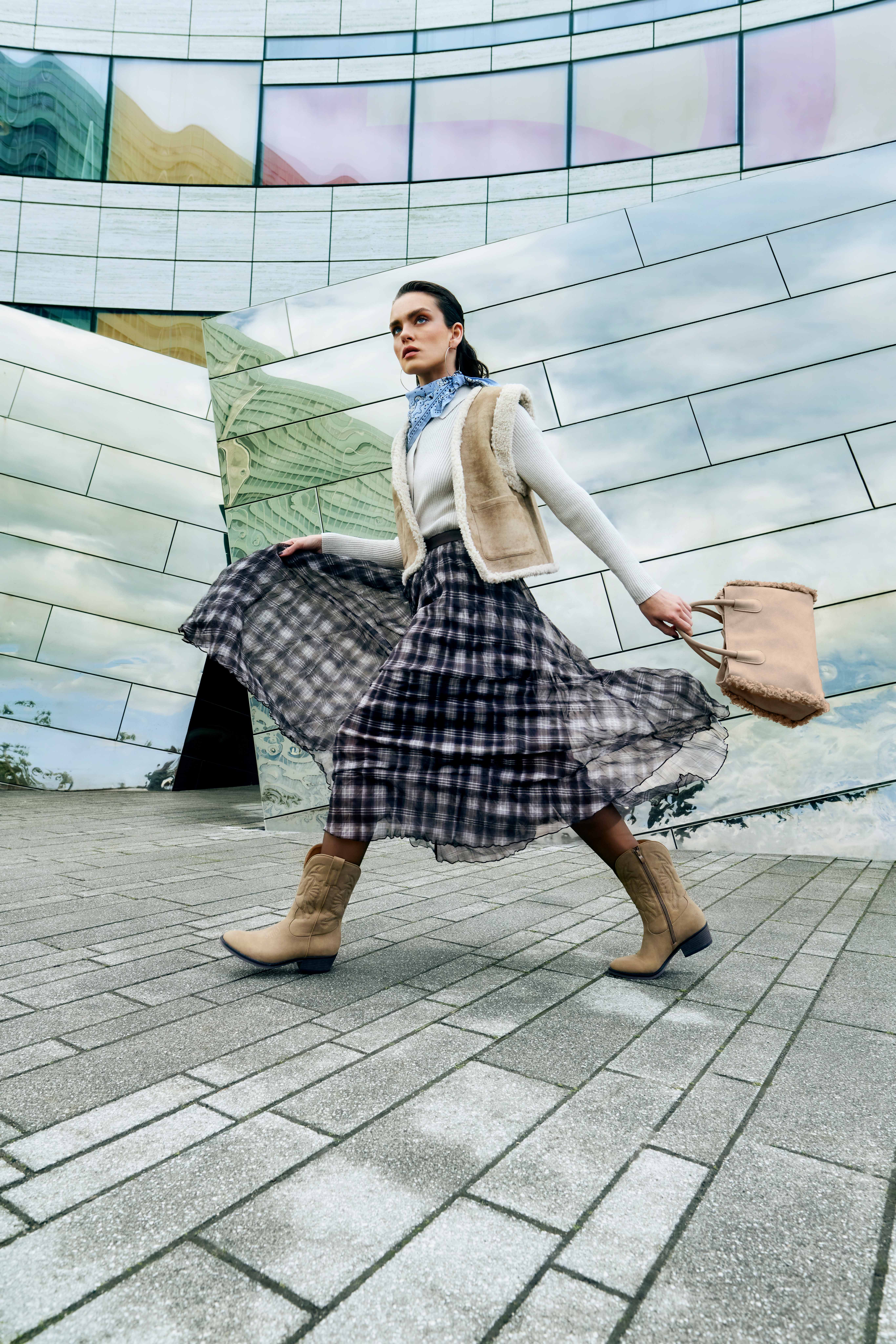 Kariertes Midikleid mit fließendem Rock, cremefarbenem Lammfell-Gilet, hellen Stiefeletten und großer Fransentasche