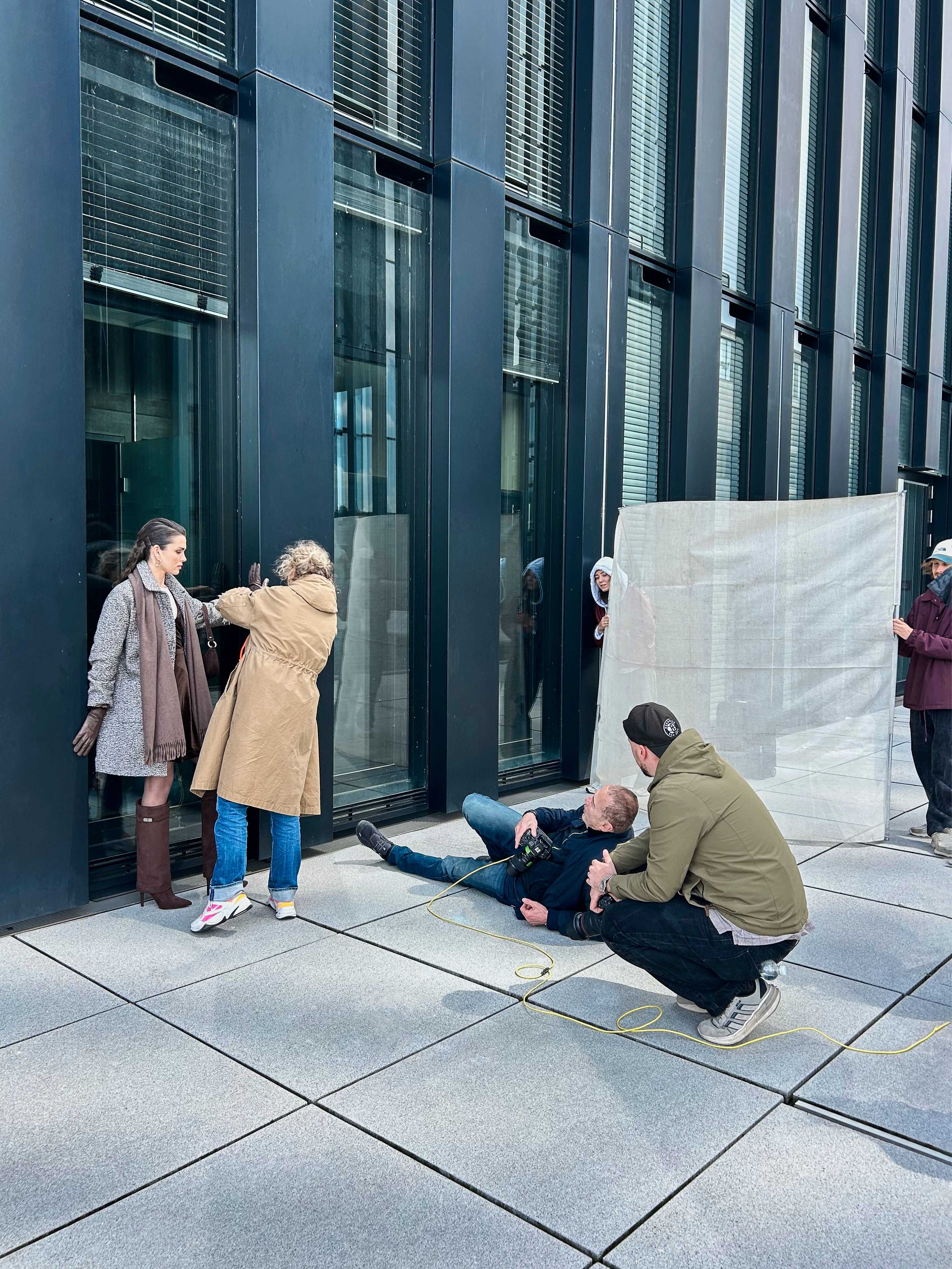 Ein Fotograf liegt auf dem Boden, während eine Frau die Pose des Models verfeinert