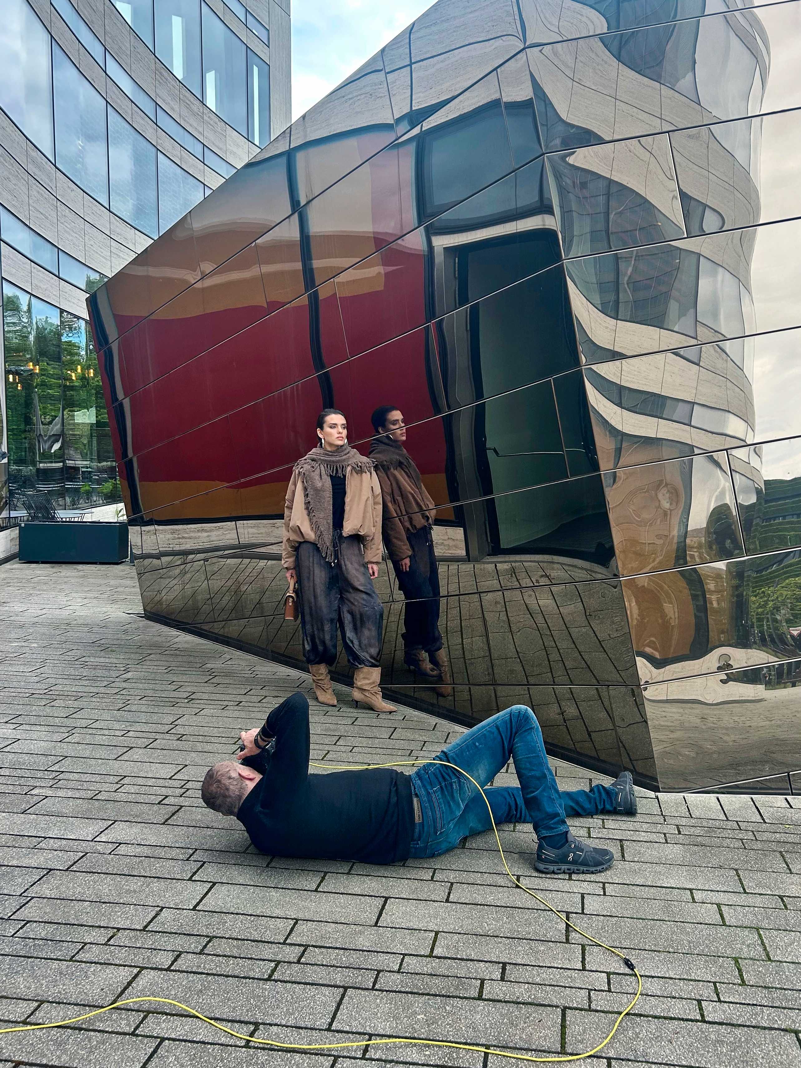 Person wird vor einer spiegelnden Gebäudefassade von einer liegenden Person fotografiert