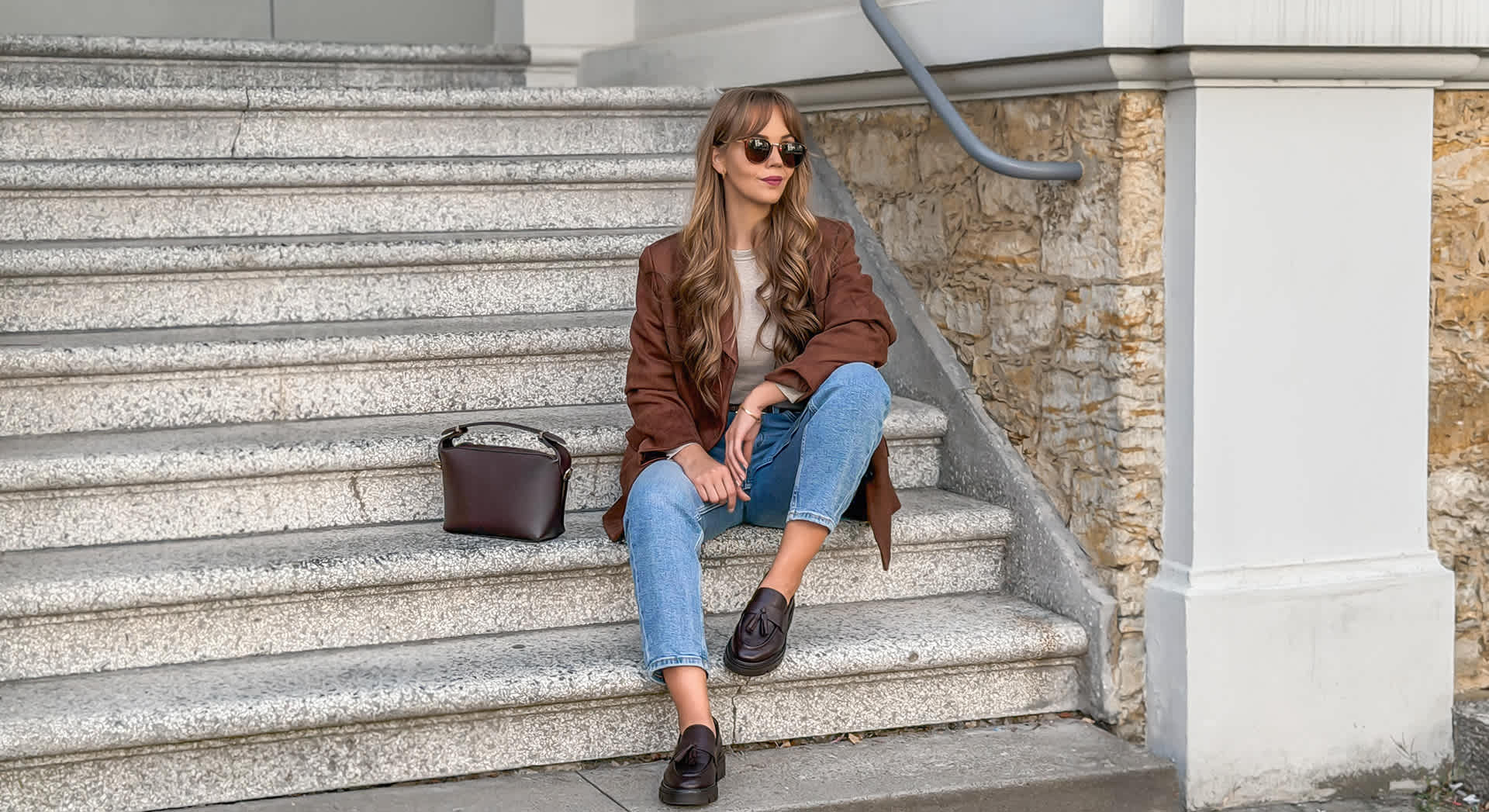 Frau sitzt auf Treppe, trägt Sonnenbrille, braunen Blazer, Jeanshose und dunkelbraune Loafer