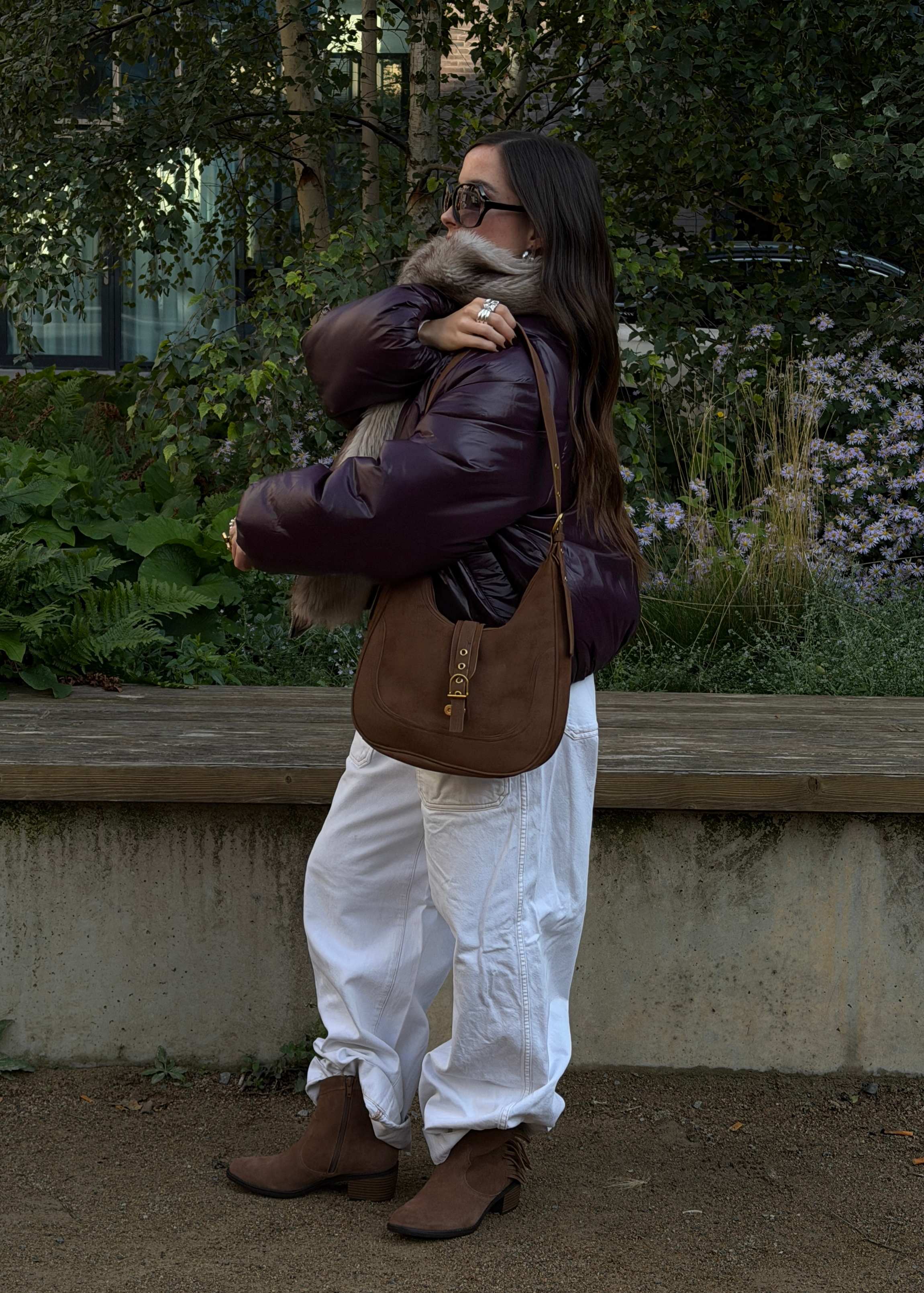 Frau in auberginefarbener Daunenjacke mit Fellkragen und weißer Baggy-Jeans trägt braune Westernstiefeletten