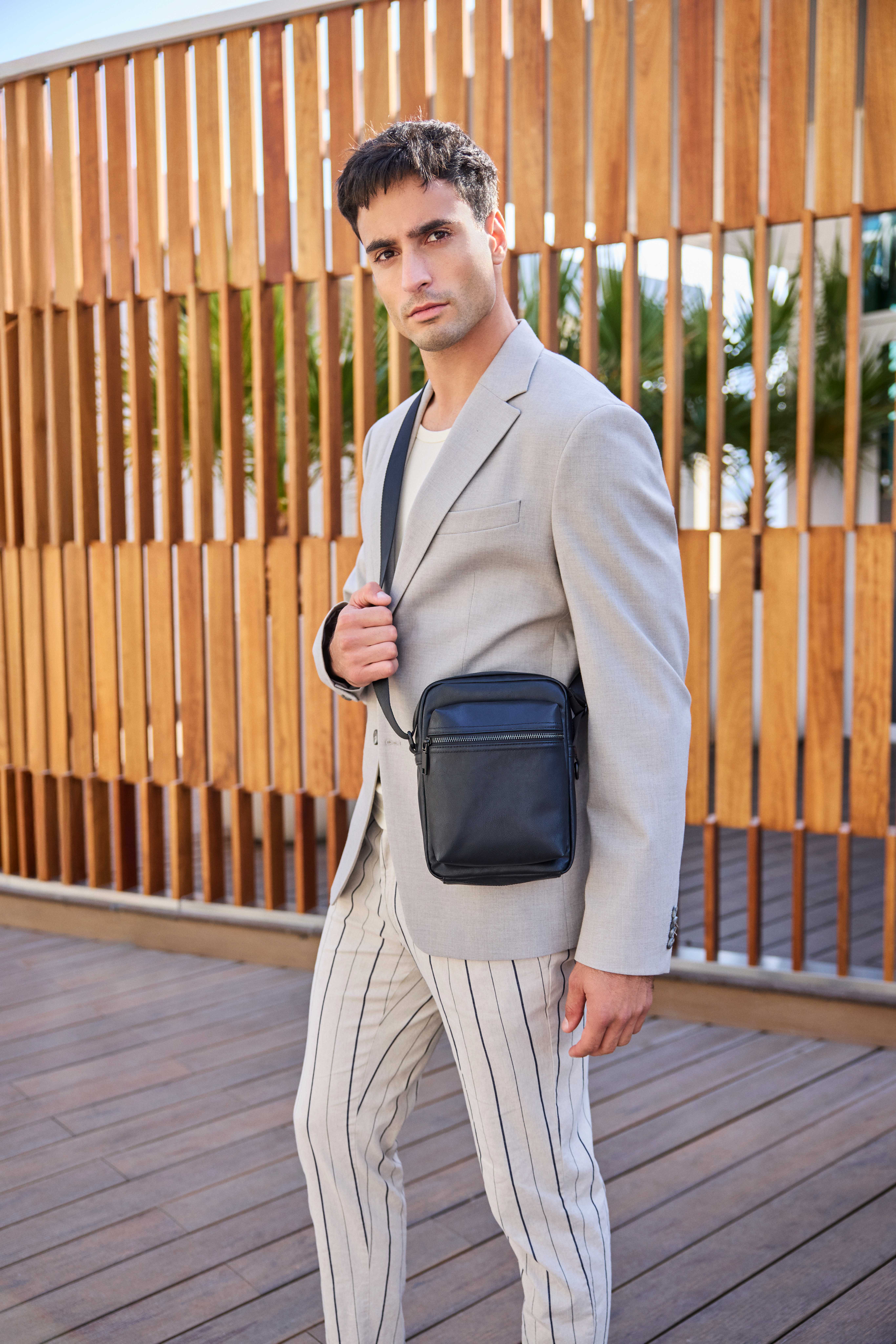 Mann in sommerlichem Business Outfit mit grauem Blazer, passender Leinenhose und dunkler Leder-Handtasche