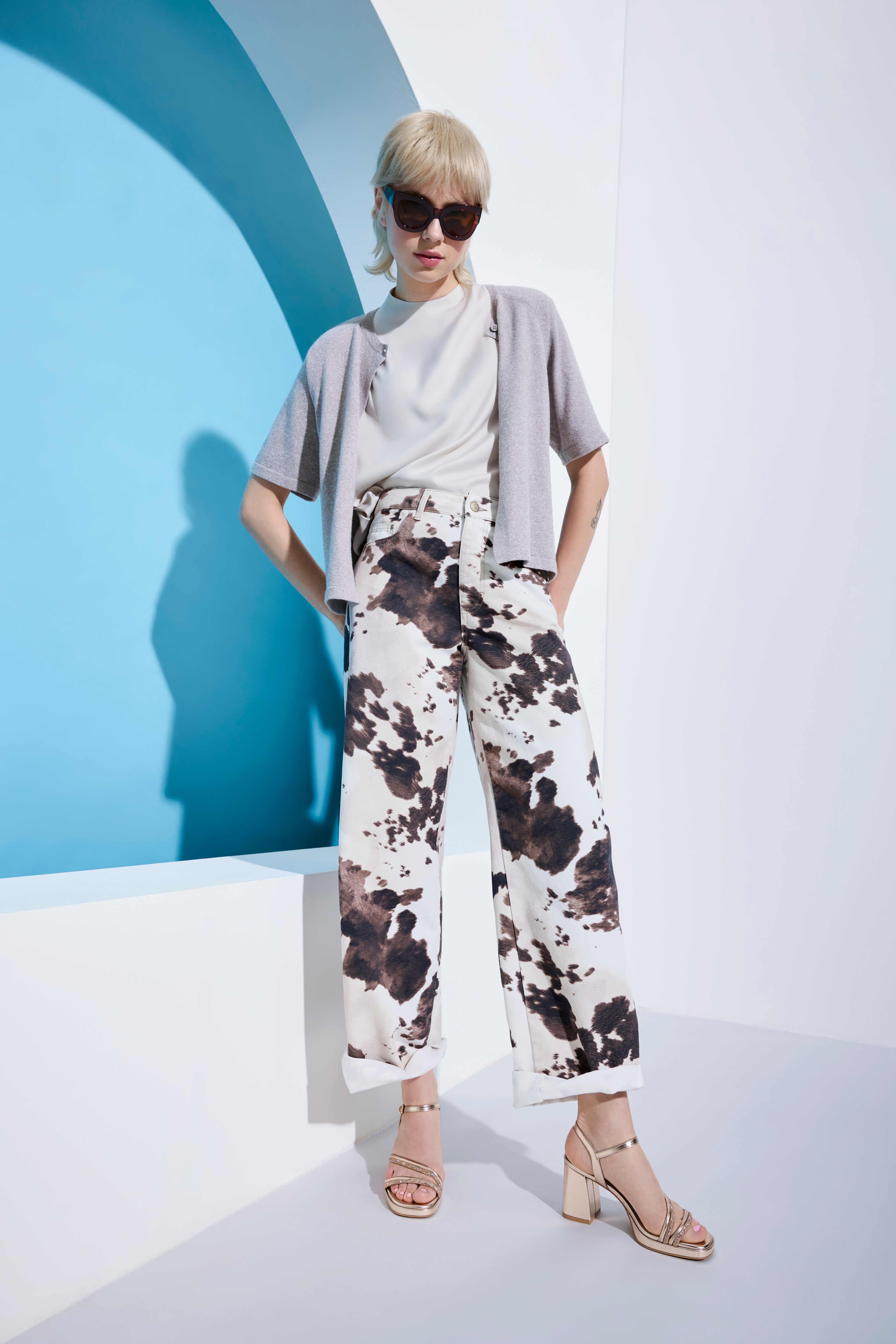 Frau mit kurzem blonden Bob, posiert lässig in grauem Top und Hose im Cowprint-Design