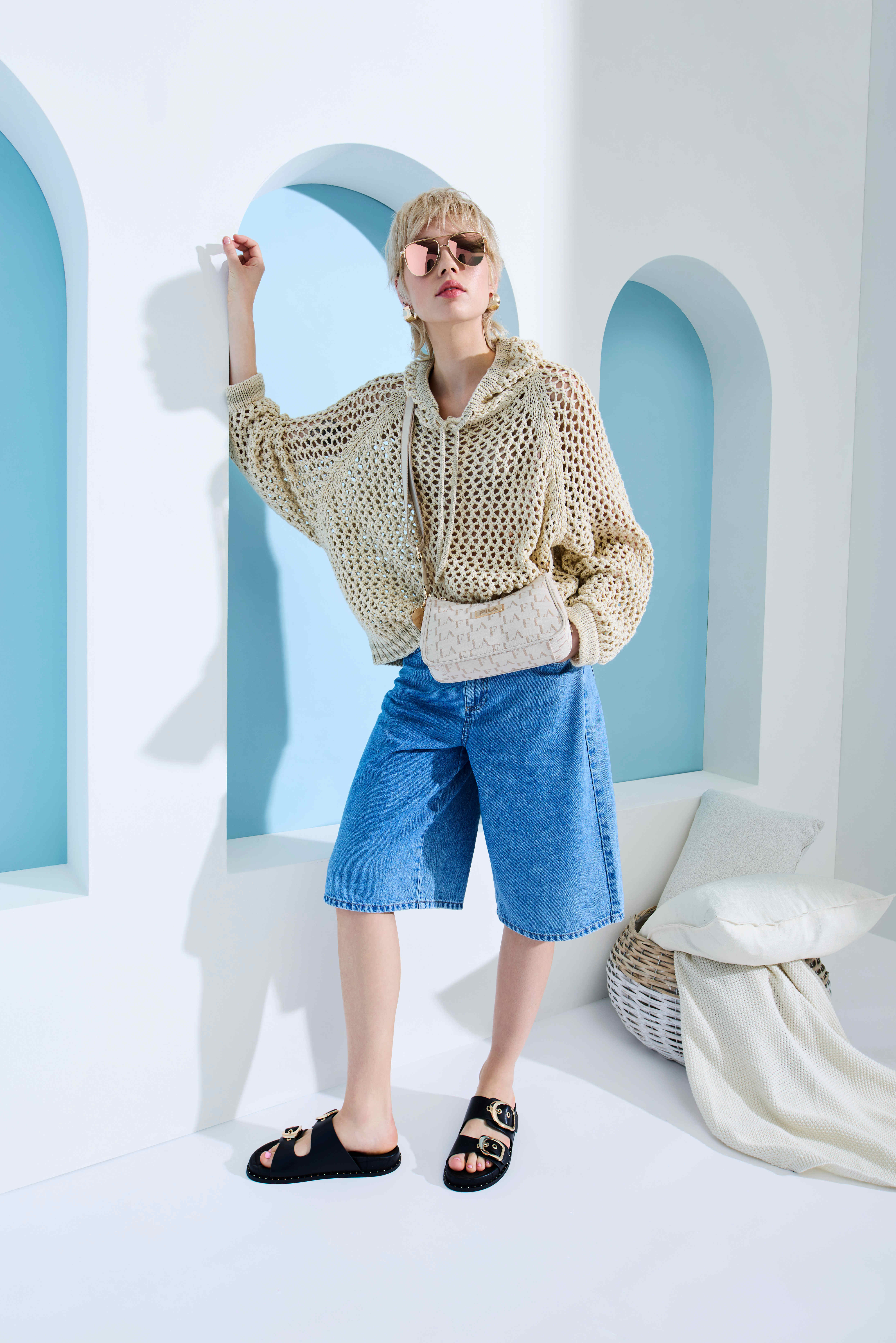 Frau in sandfarbenem Strick-Top, blauen Shorts und schwarzen Sandalen