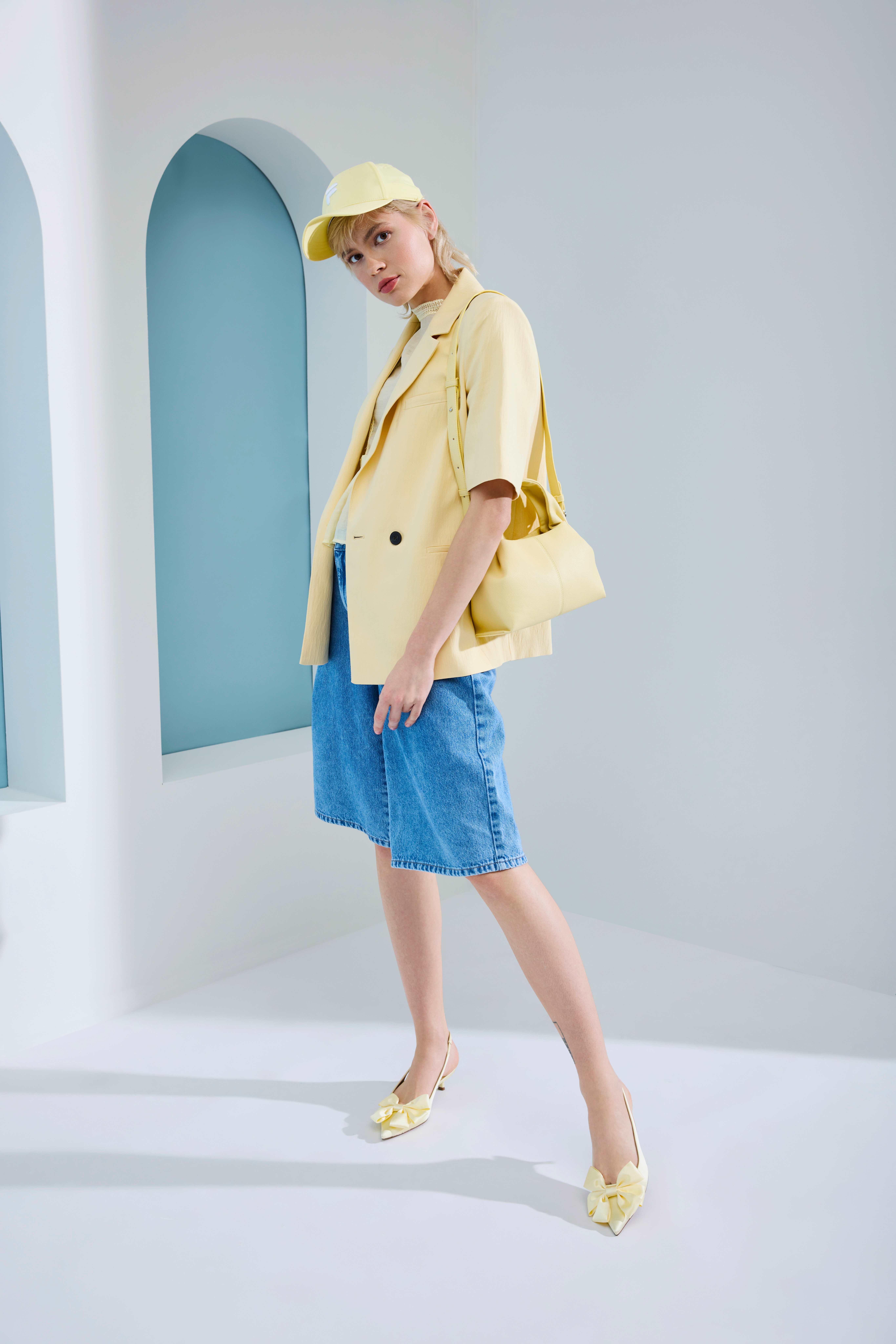 Frau mit gelbem Hemd und passender Cap, kombiniert mit blauer Jeans-Shorts 