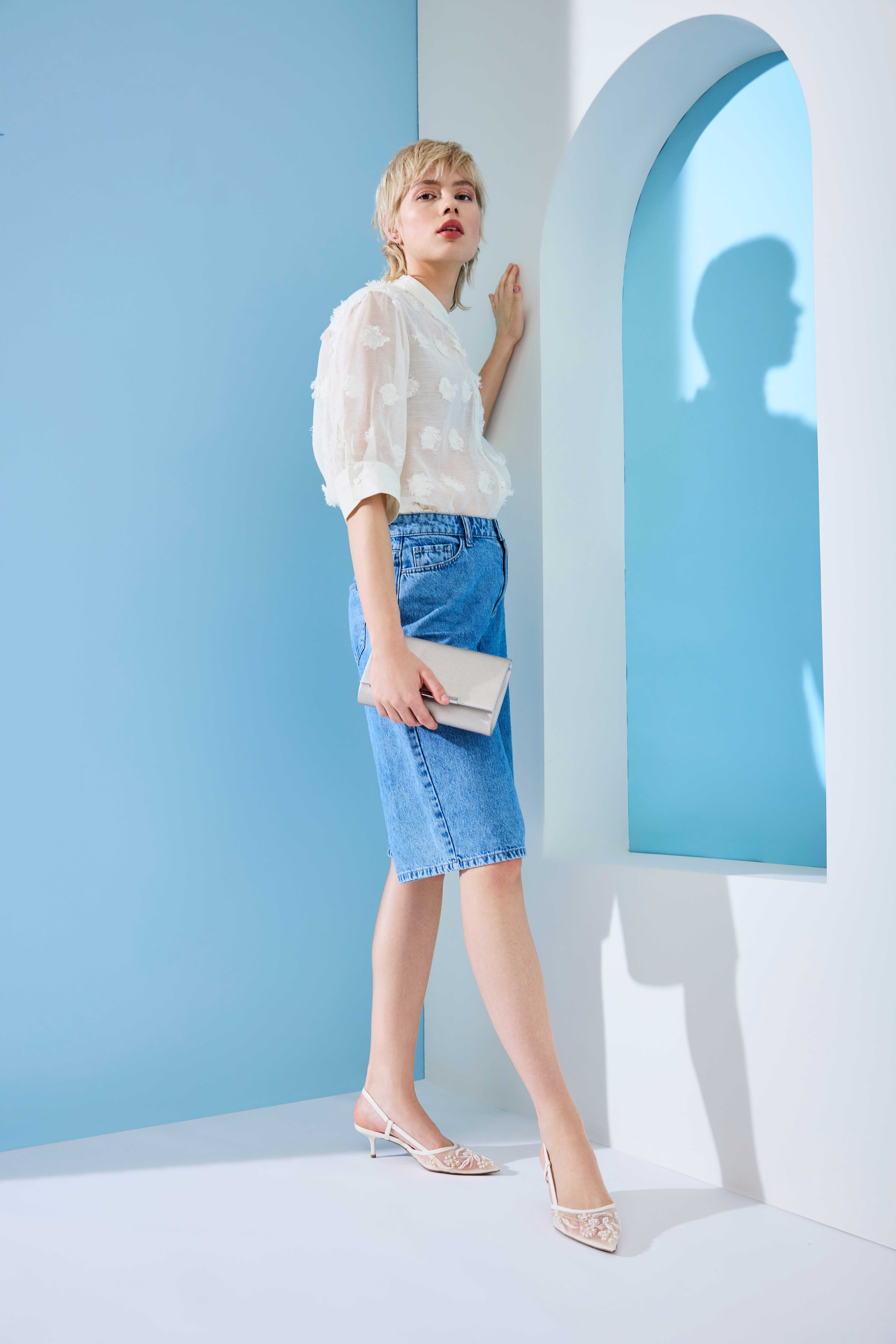 Blonde Frau in blauem Pencil Skirt und weißer Bluse, mit weißer Clutch in der Hand