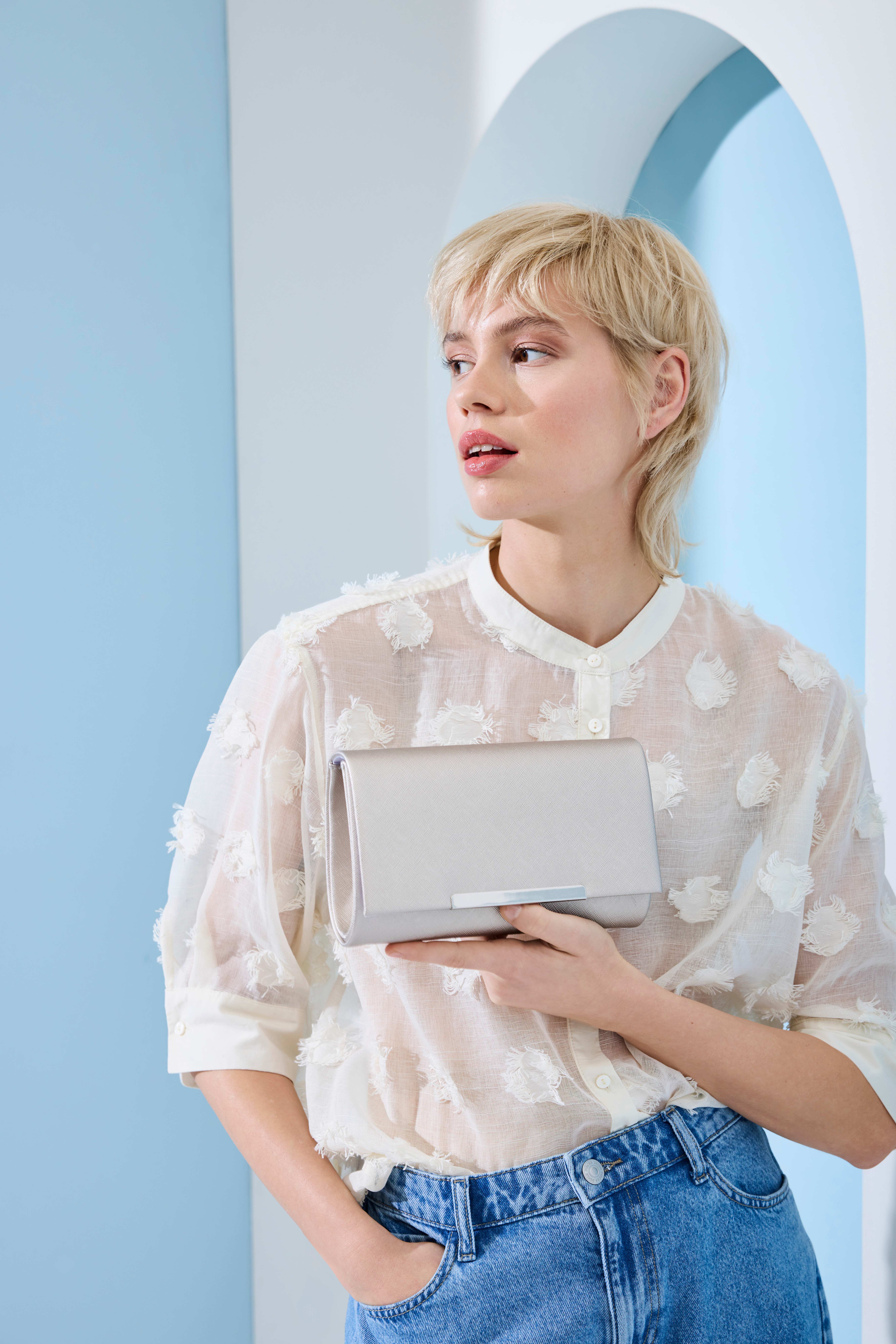 Blonde Frau mit blass-weißer Bluse und weißer Clutch in der Hand