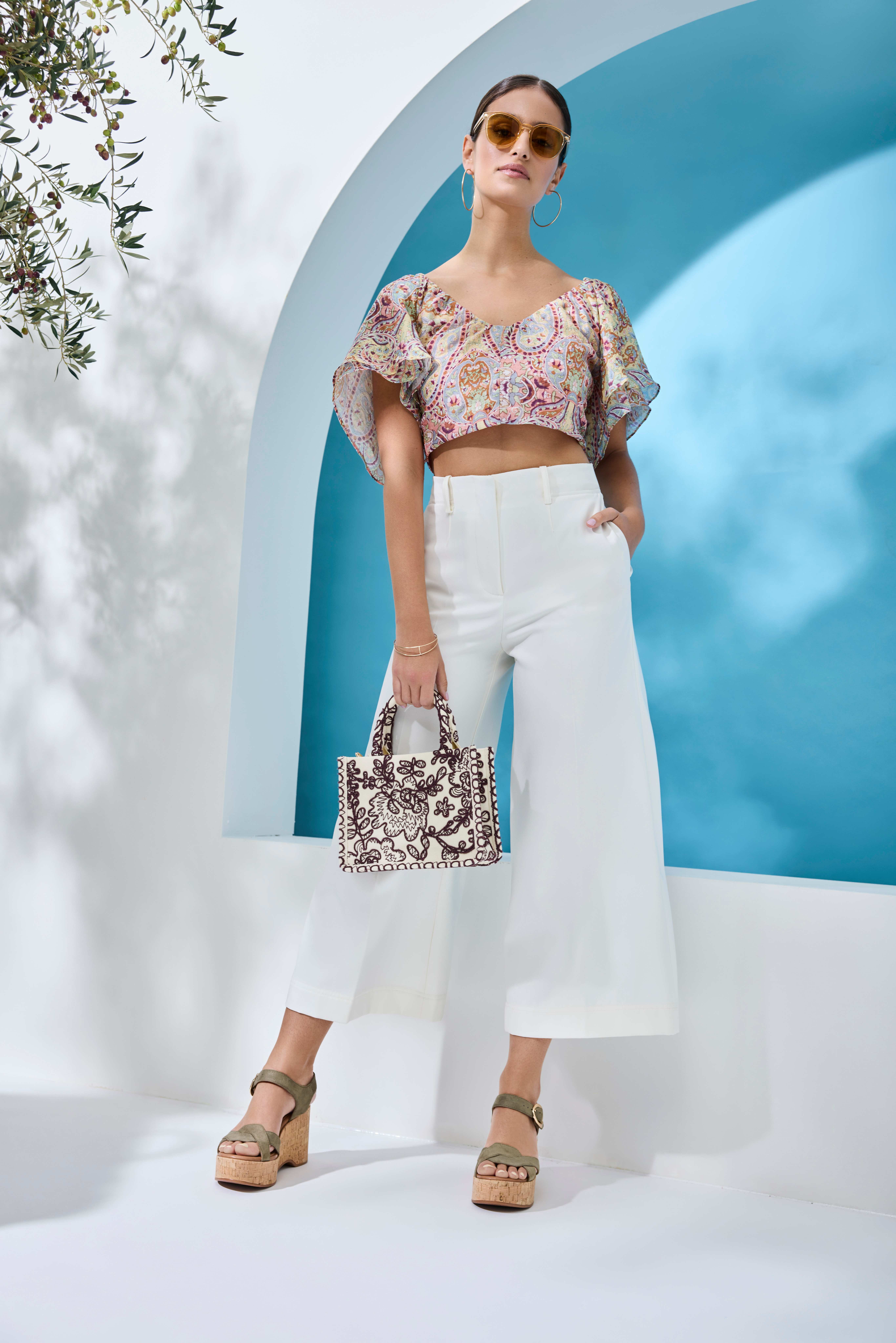 Frau mit Sonnenbrille trägt Blumentop mit weißer Culotte und Plateauschuhen