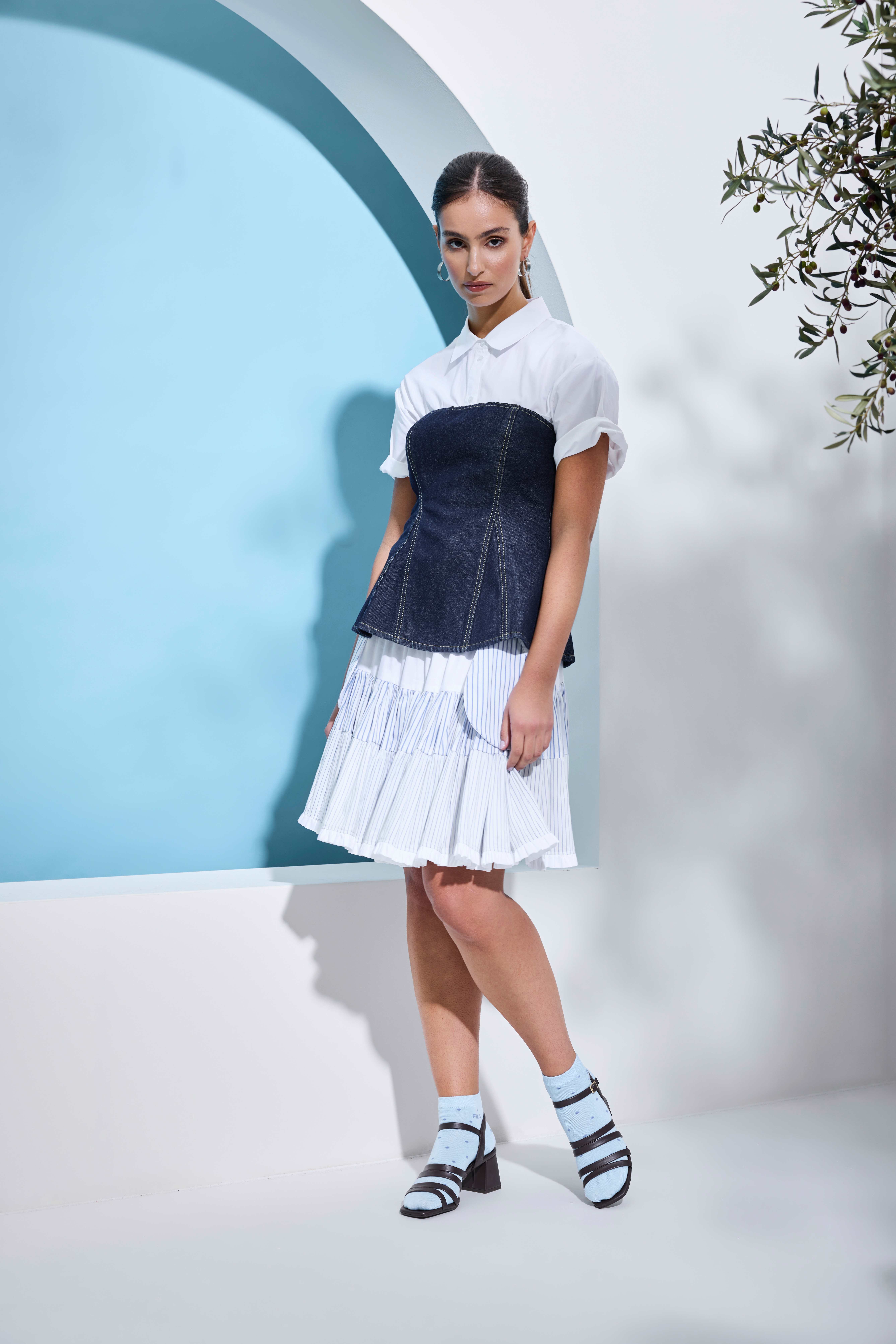 Person mit Denim‑Corsage über weißem Kleid, kombiniert mit Riemchensandaletten mit Blockabsatz