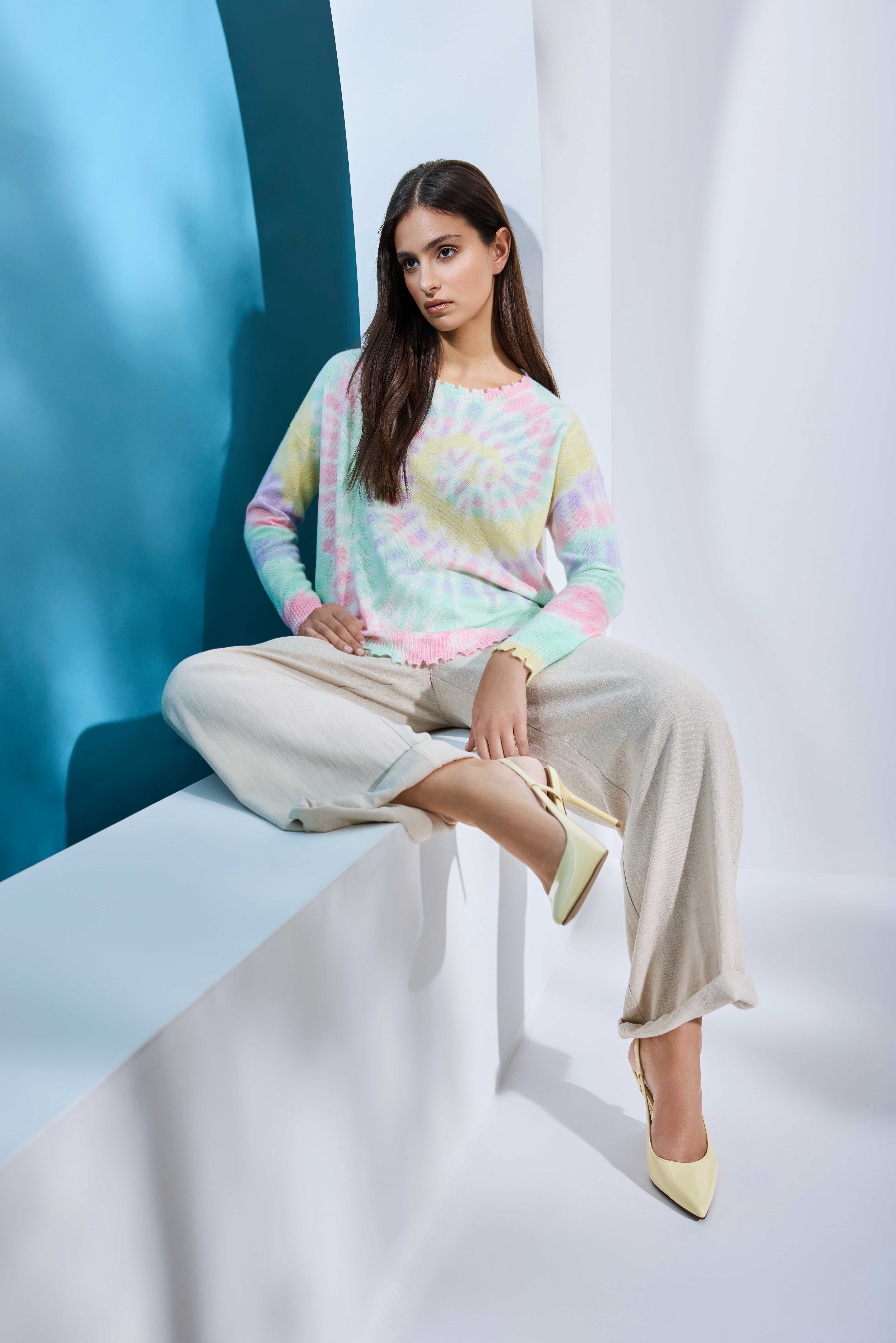 Frau in Candy Color-Top, sitzt in Torbogen, trägt lässige Hose und Pumps