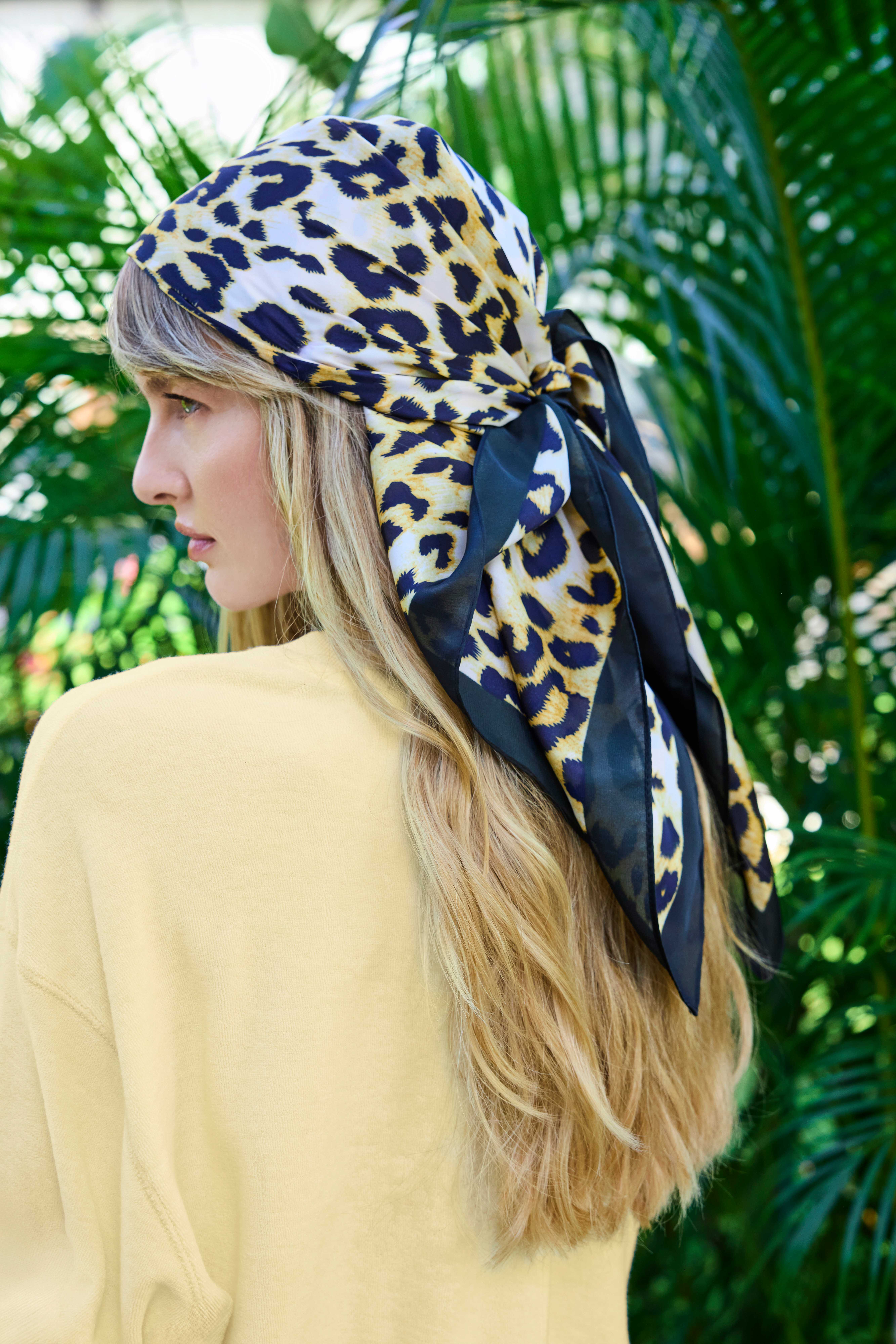 Blonde Frau in Palmenkulisse, trägt Sommertuch im Leo-Print