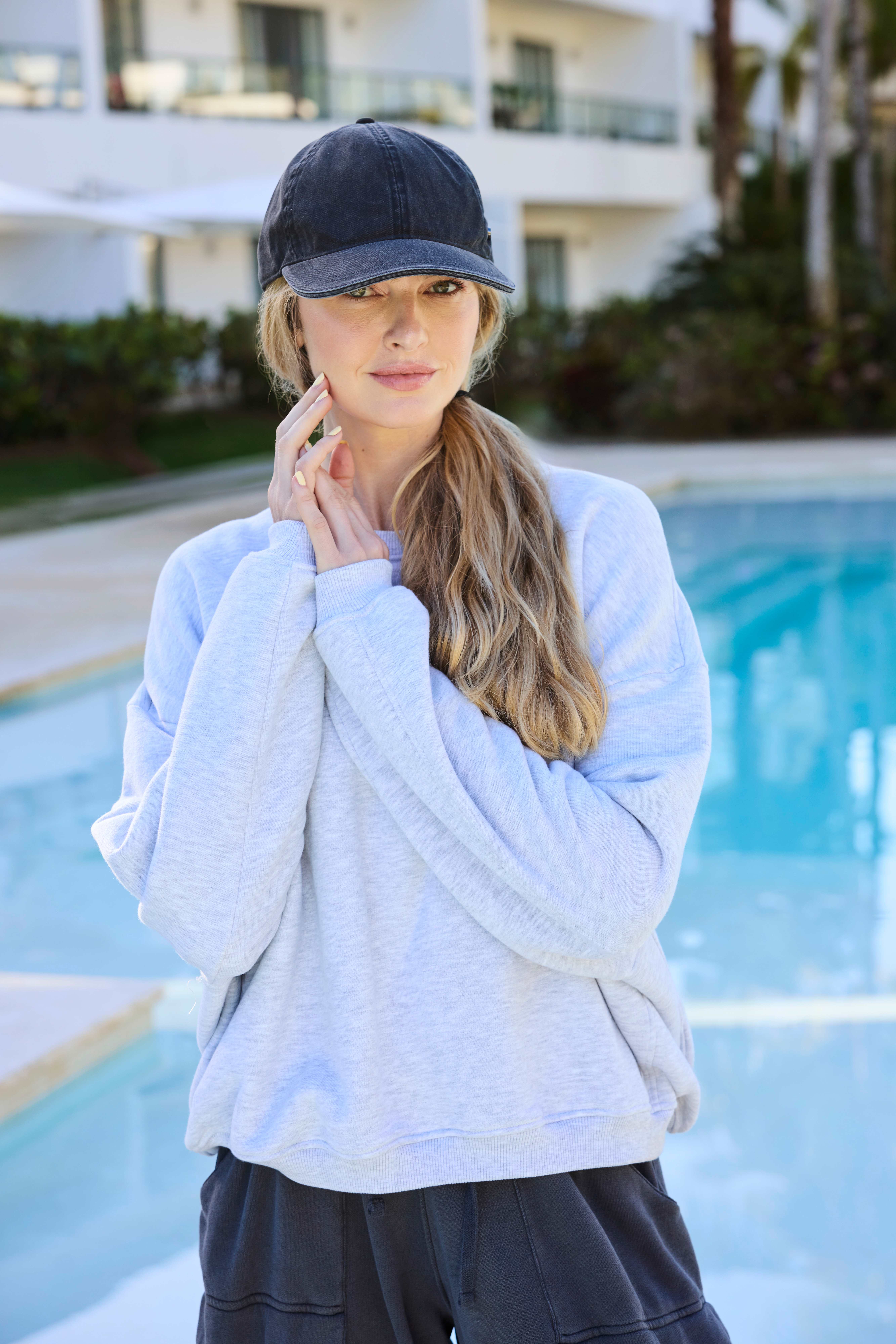 Frau mit Cap und hellblauem Shirt, steht im Tomboy Look vor Pool