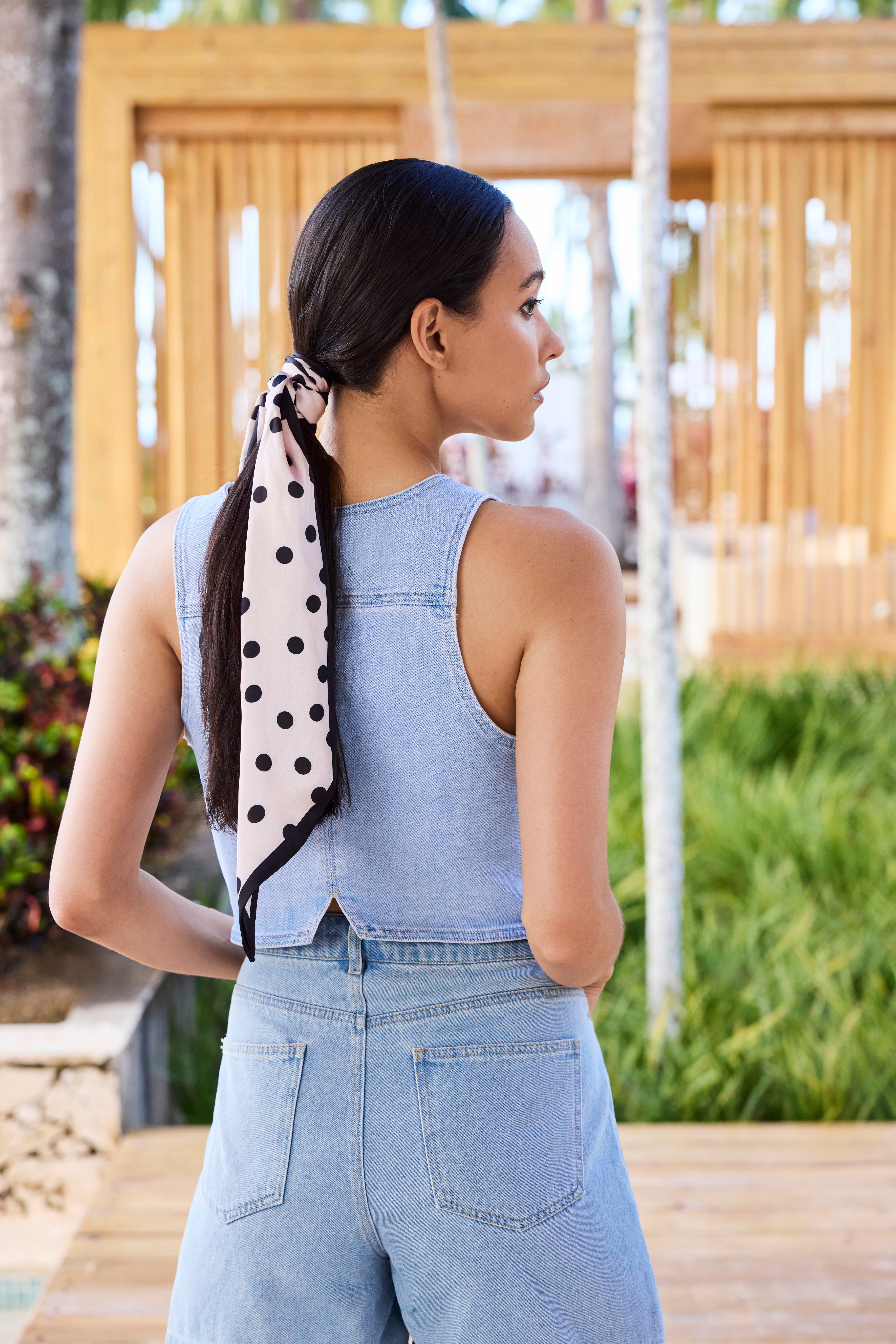 Frau in Jeans-Look, steht mit dem Rücken zum Betrachter, mit Polka Dot-Tuch im Haar
