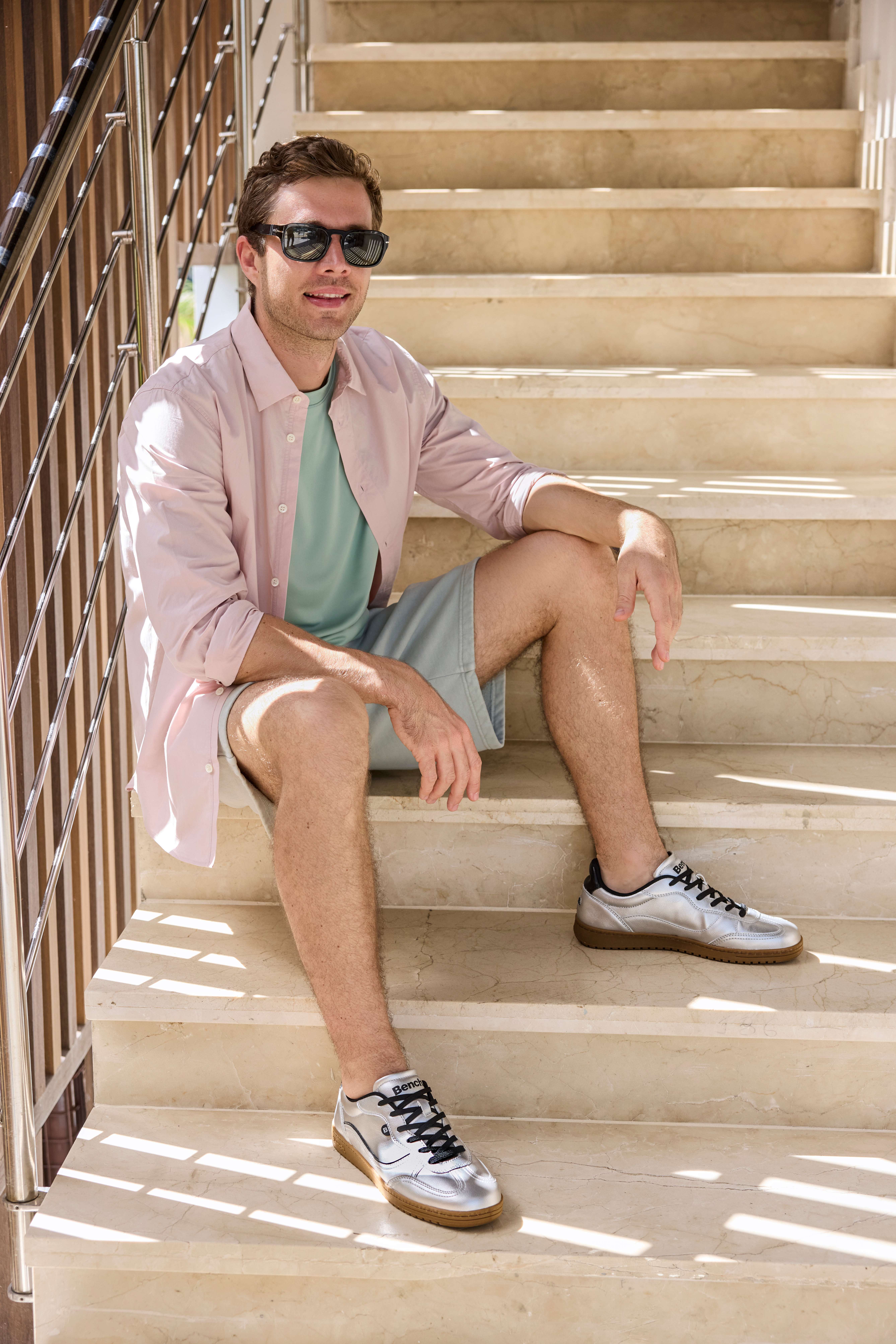 Mann in lässigem Sommer-Outfit, mit Hemd und Shorts, sitzend auf Steintreppe