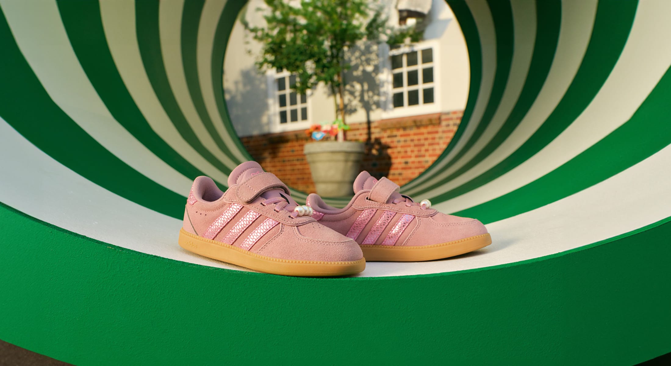 Sneaker Adidas rosa con effetto pelle scamosciata e suola in gomma, in uno scenario circolare da palestra